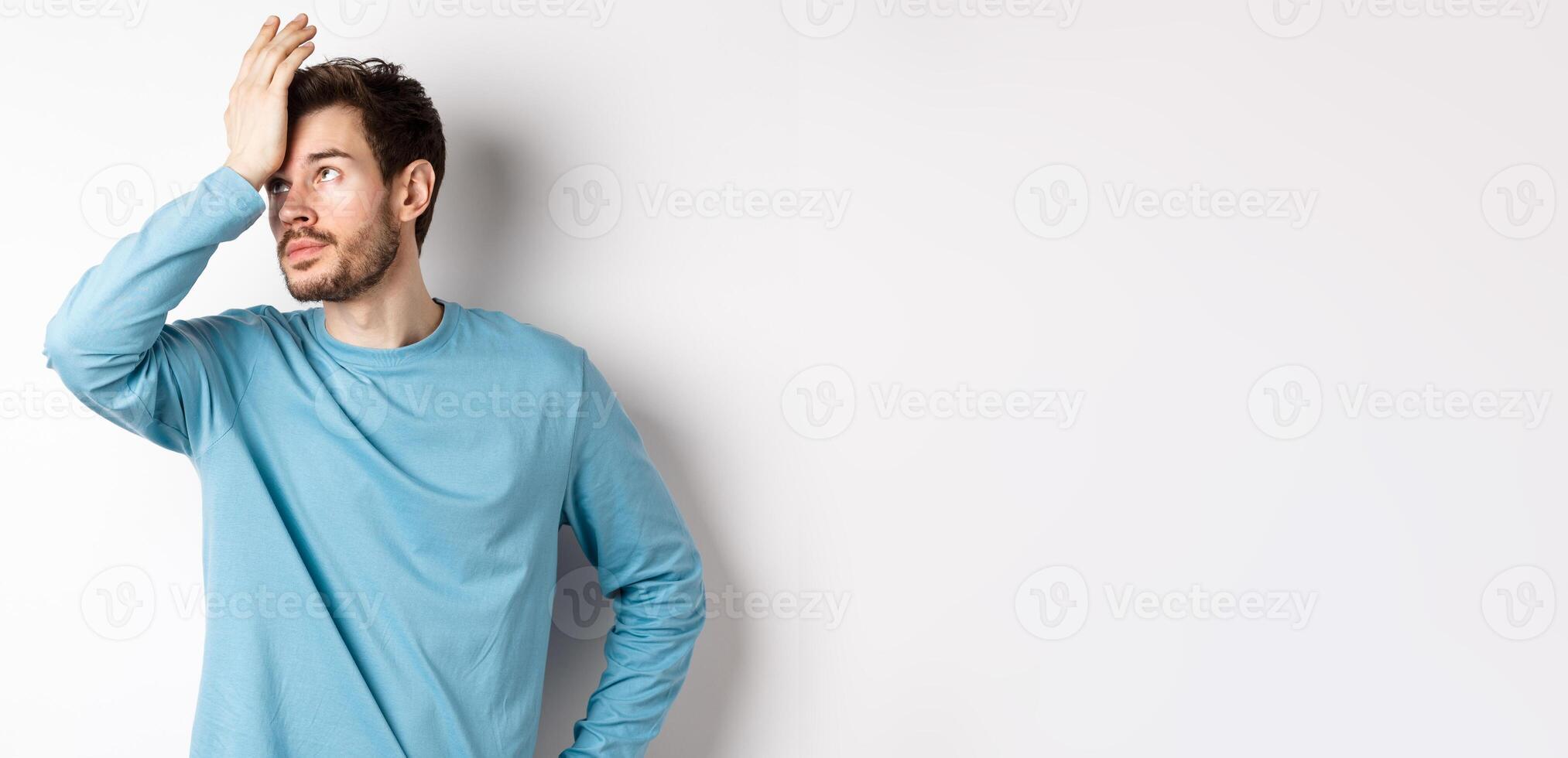 Annoyed young man with beard, roll eyes and making facepalm, pissed-off with something, standing irritated on white background photo