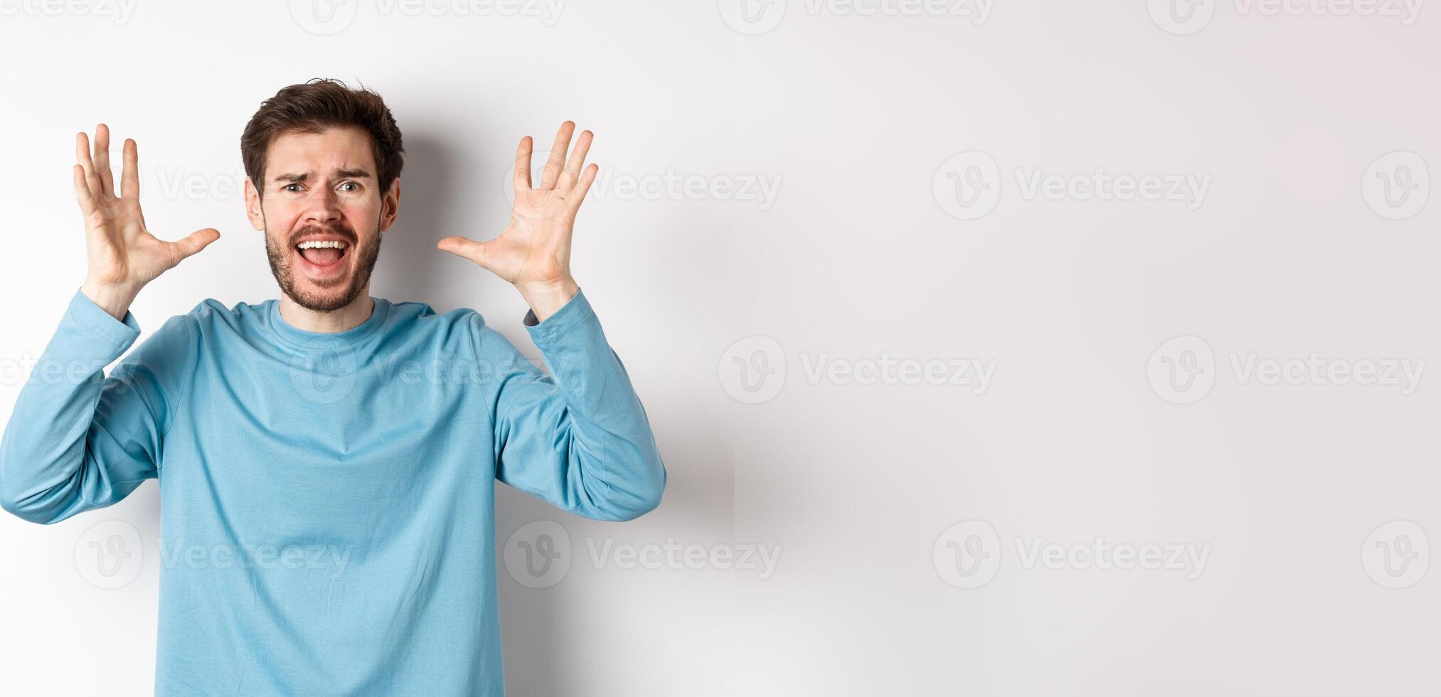 Image of freaked out young man screaming and shaking hands, shouting at camera frustrated or worried, panicking over white background photo