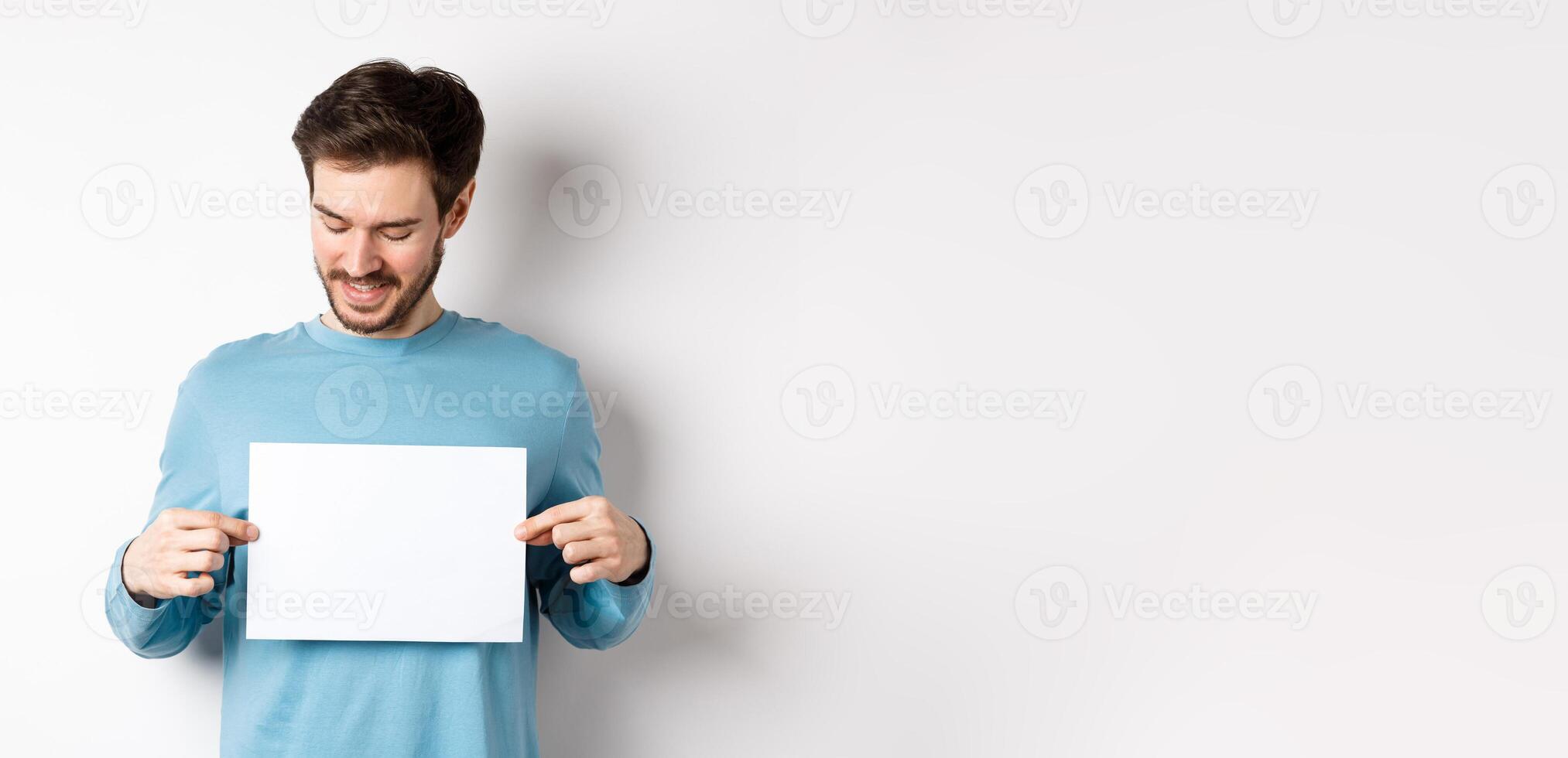 Young caucasian man looking at empty paper, reading logo, standing on white background photo