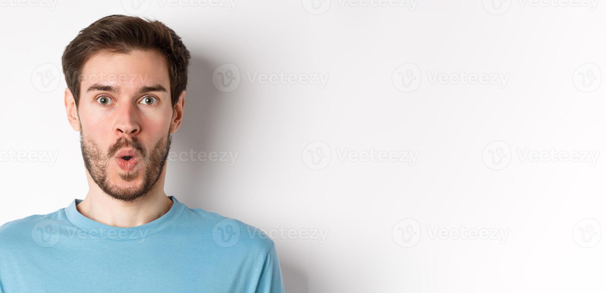 Close-up of surprised man face, saying wow and staring at camera amazed, standing on white background photo