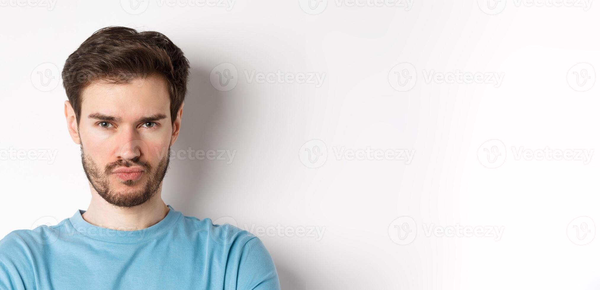 Close-up of grumpy young man grimacing, sulking and making offended face, standing upset over white background photo