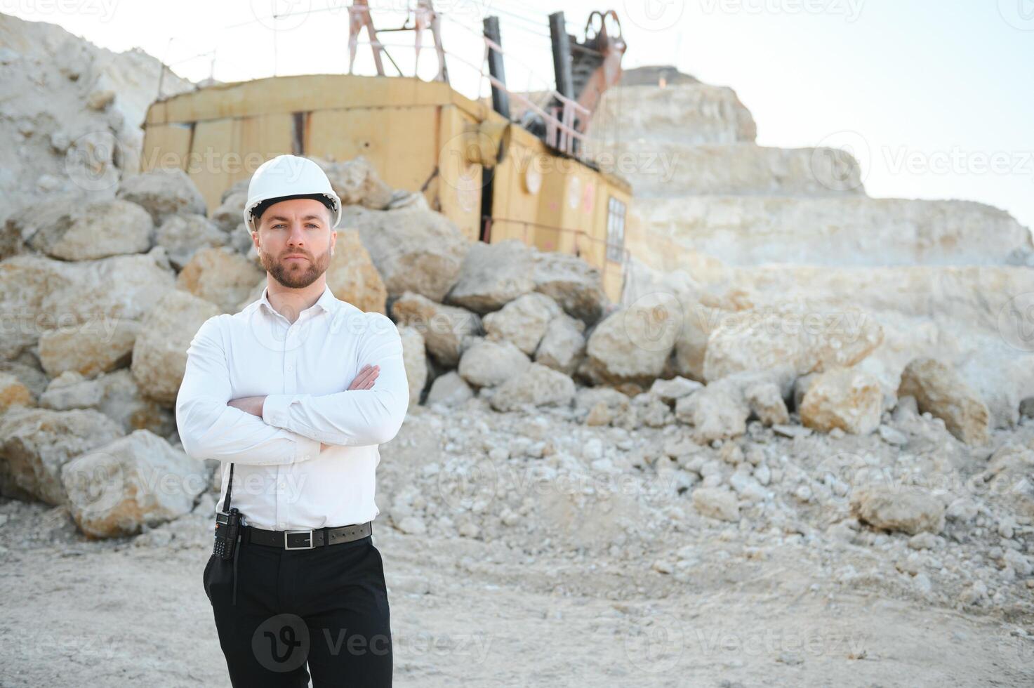 A worker in a helmet stands on the background of an excavator in a quarry photo