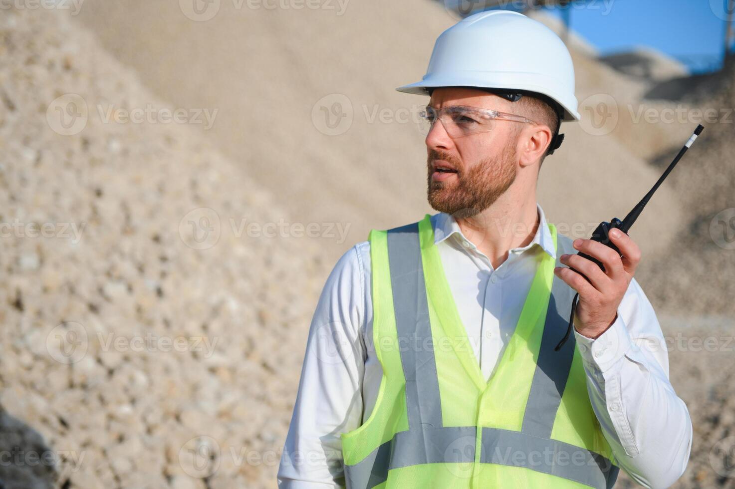 A worker in a hard hat stands with a walkie-talkie at a stone crushing plant. photo