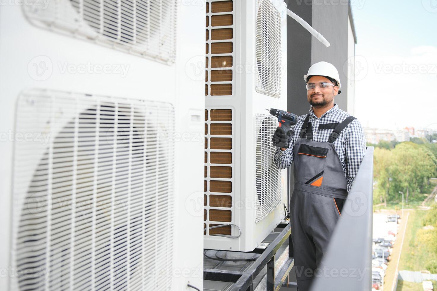 Young indian man repairman checking an outside air conditioner unit photo