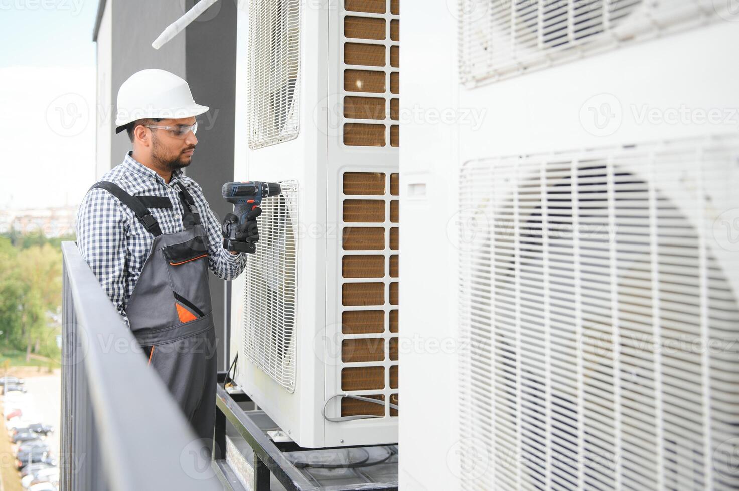 Indian Repairman in uniform installing the outside unit of air conditioner photo
