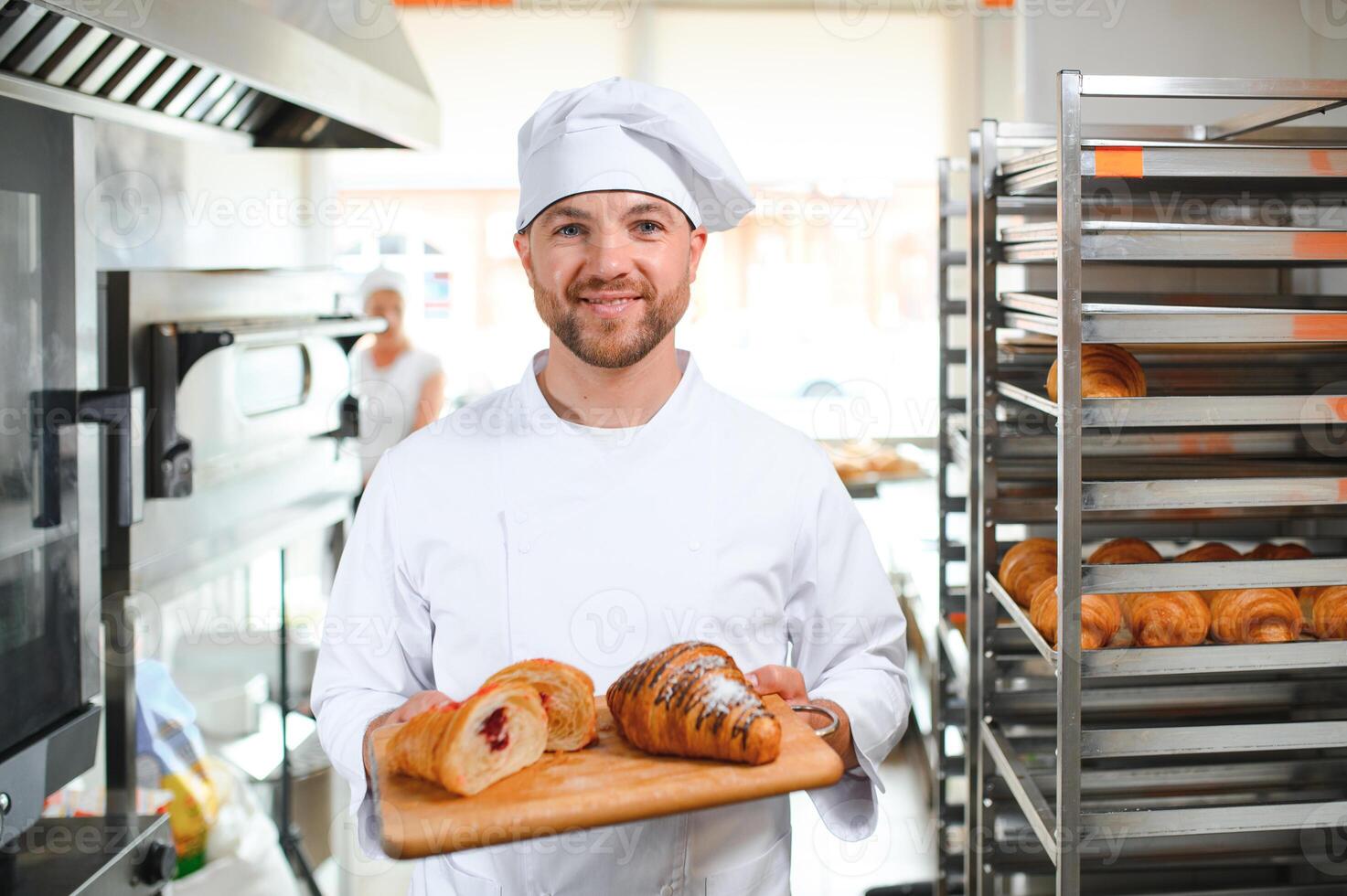 A young handsome male baker holds a tray with French croissants in front of a bakery and smiles photo