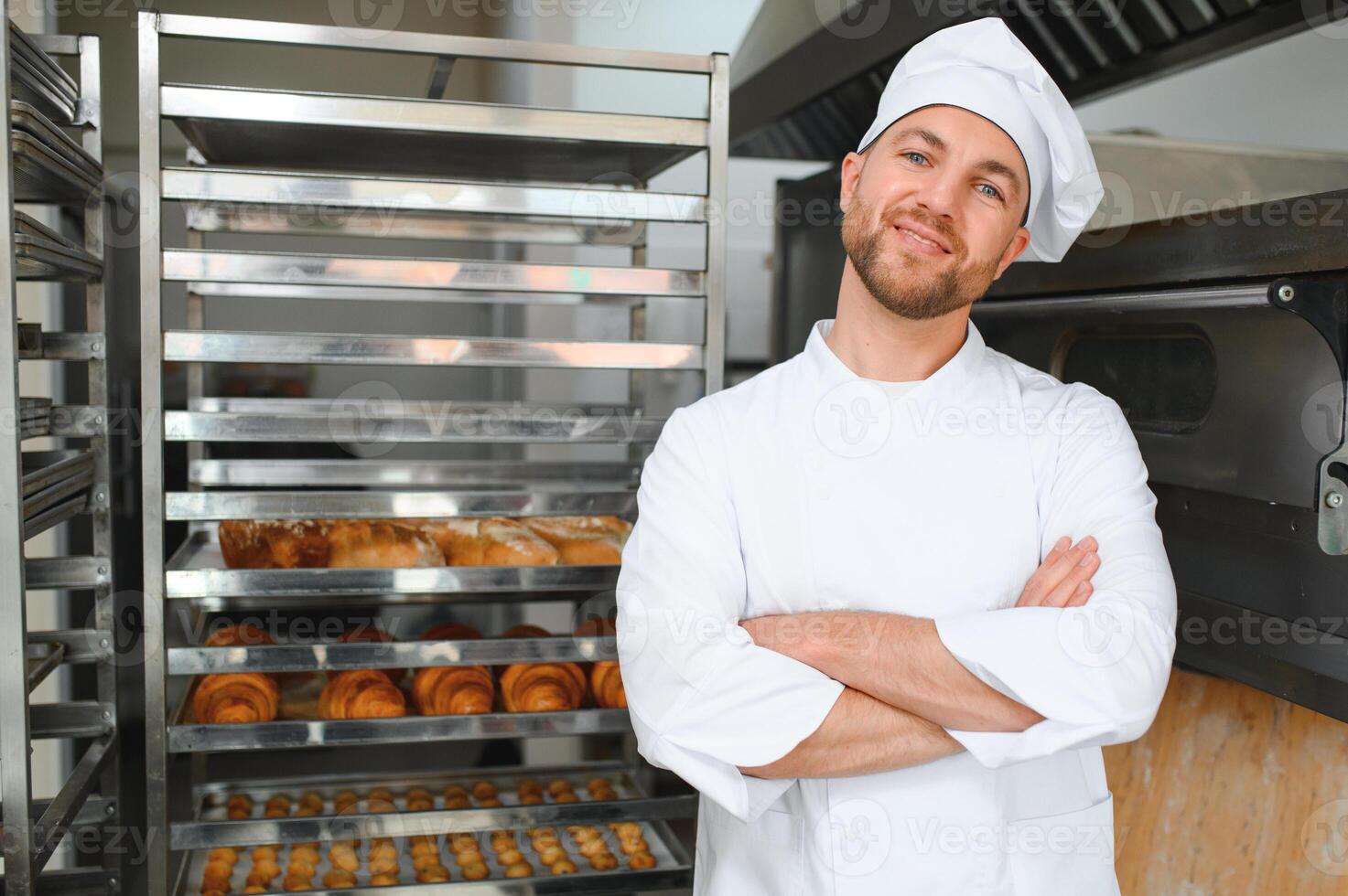 Portrait of handsome baker at the bakery with breads and oven on the background photo