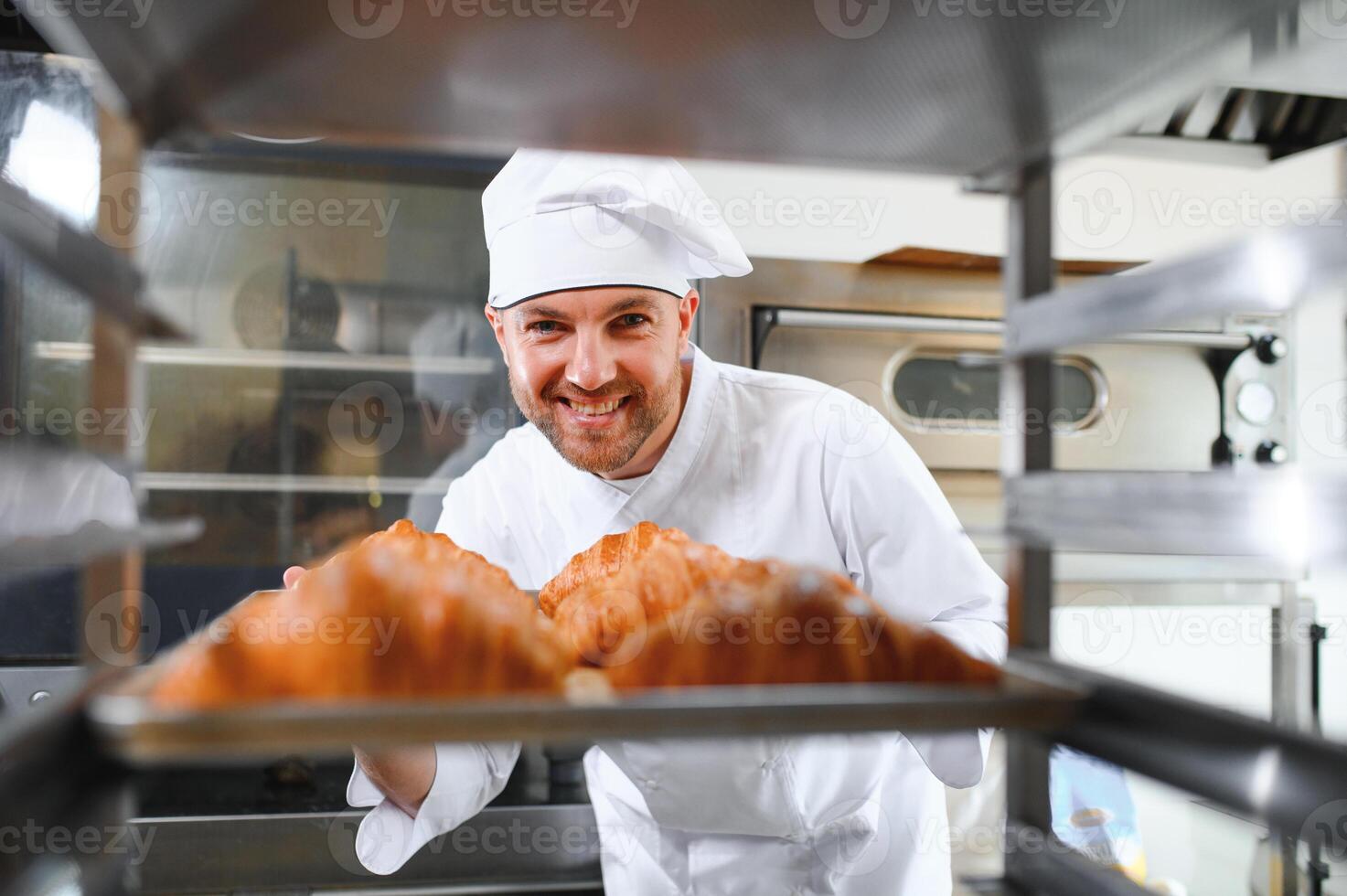 A young handsome male baker holds a tray with French croissants in front of a bakery and smiles photo