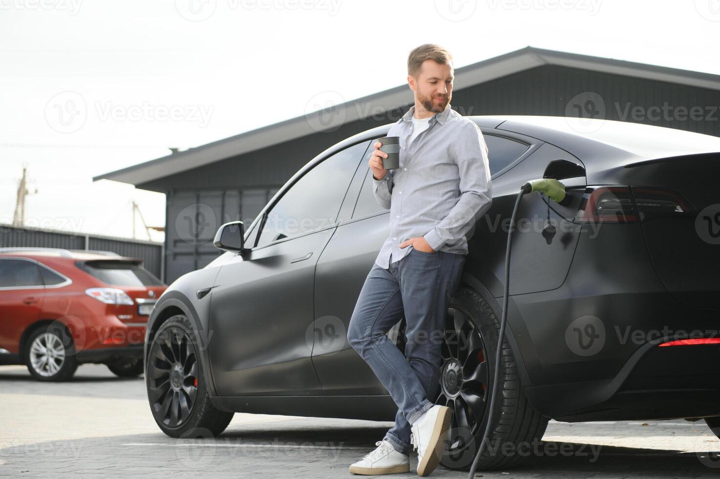 Handsome man drinking coffee while charging electric car photo
