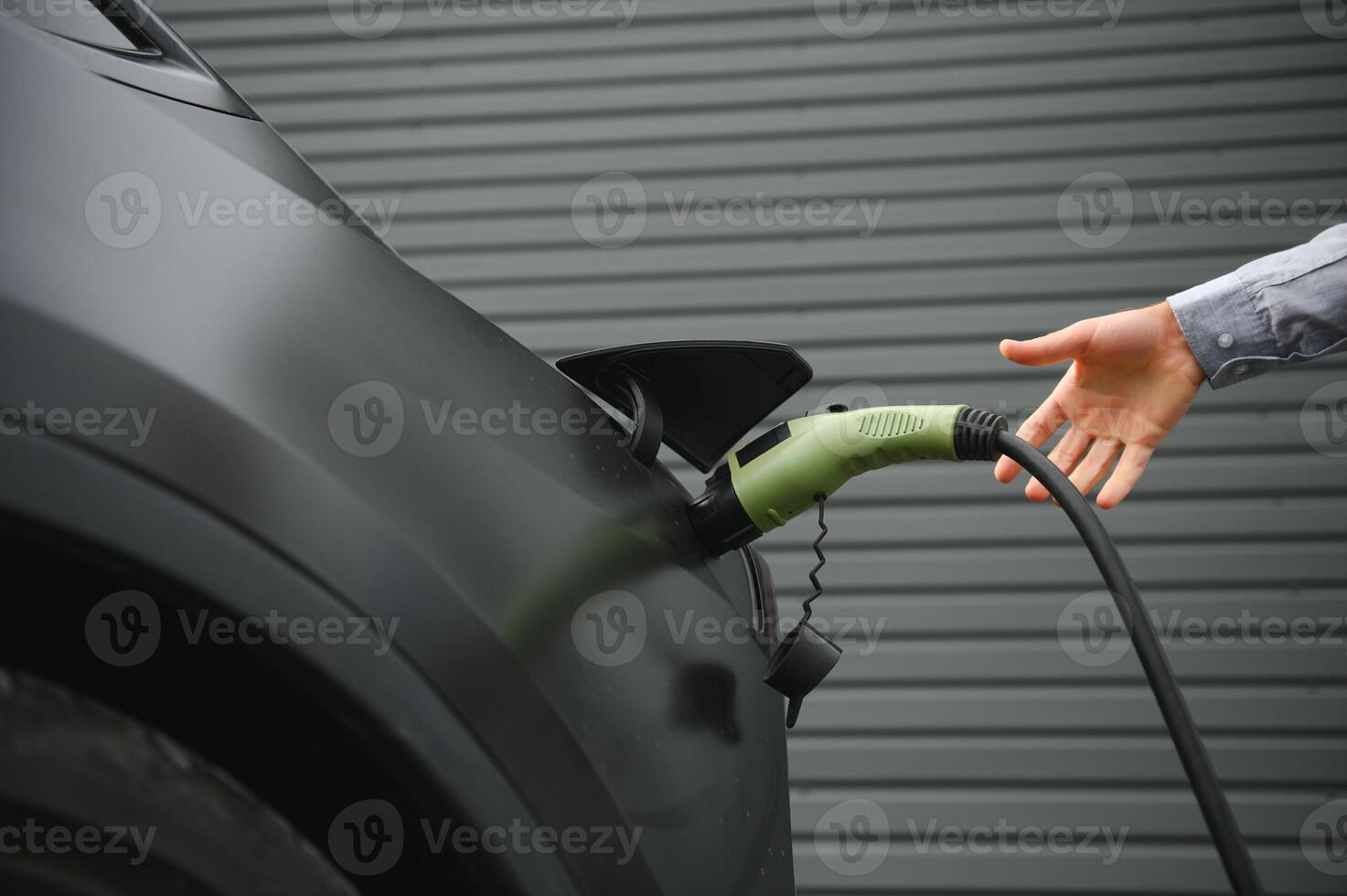A man charges an electric car and checks the charge level on a smartphone photo