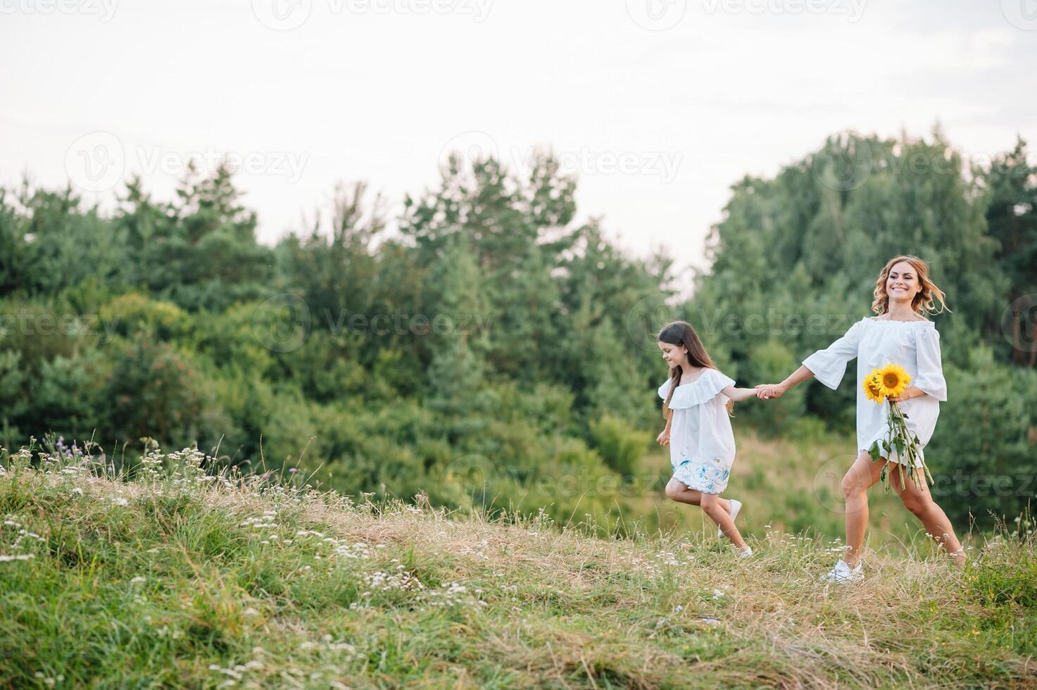 Cheerful mother and her little daughter having fun together in the summer background. Happy family in the nature background. Cute girls with colorful flowers. photo