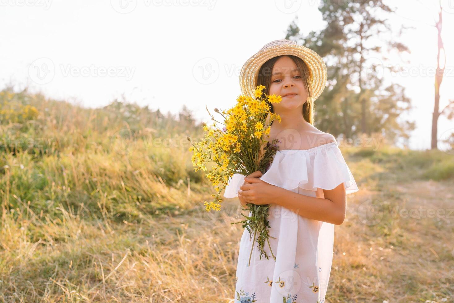 Outdoor shot of pleasant looking young girl with tanned healthy skin, dressed in white dress and summer hat, poses in park with confident satisfied expression, likes recreation. Beautiful young woman. photo