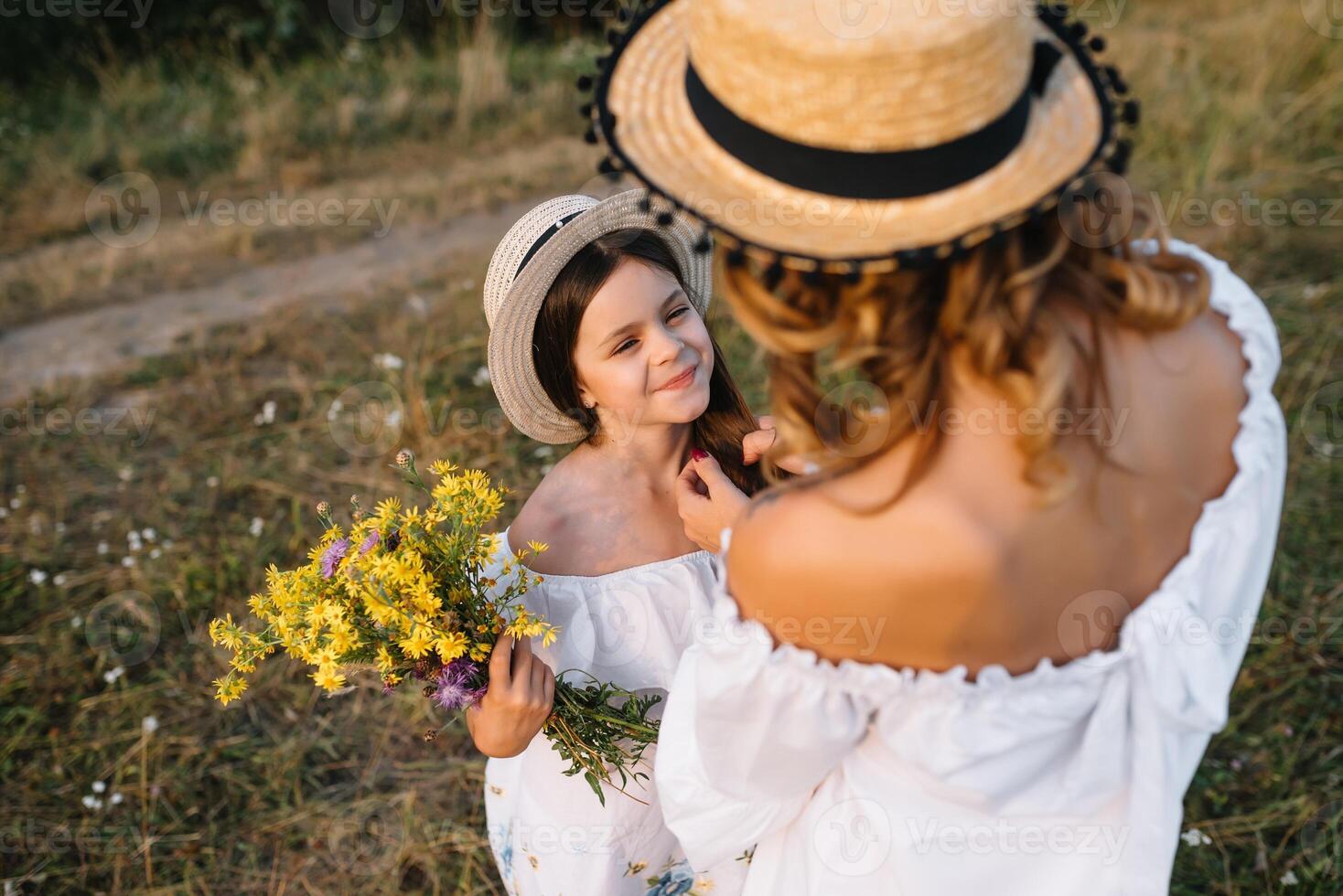 Cheerful mother and her little daughter having fun together in the summer background. Happy family in the nature background. Cute girls with colorful flowers photo