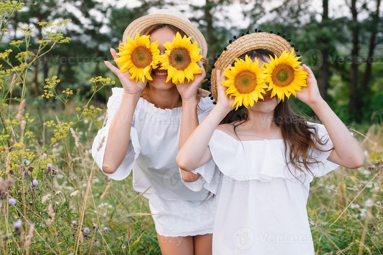 Cheerful mother and her little daughter having fun together in the summer background. Happy family in the nature background. Cute girls with colorful flowers photo