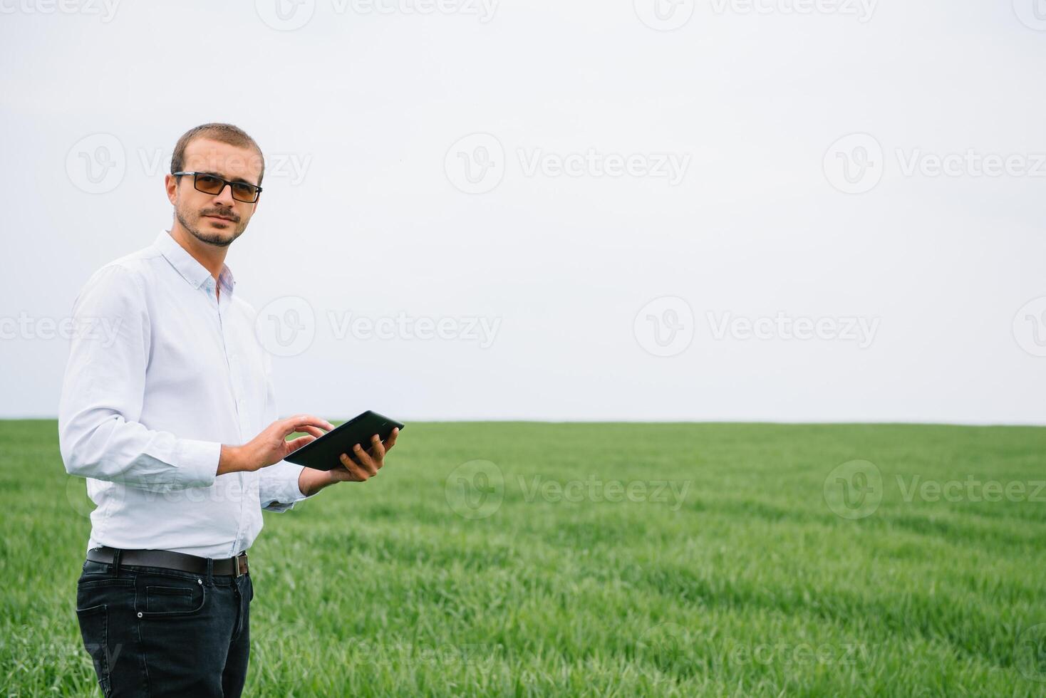 Young agronomist holds tablet touch pad computer in green wheat field. Agribusiness concept. agricultural engineer standing in a wheat field with a tablet in summer. photo
