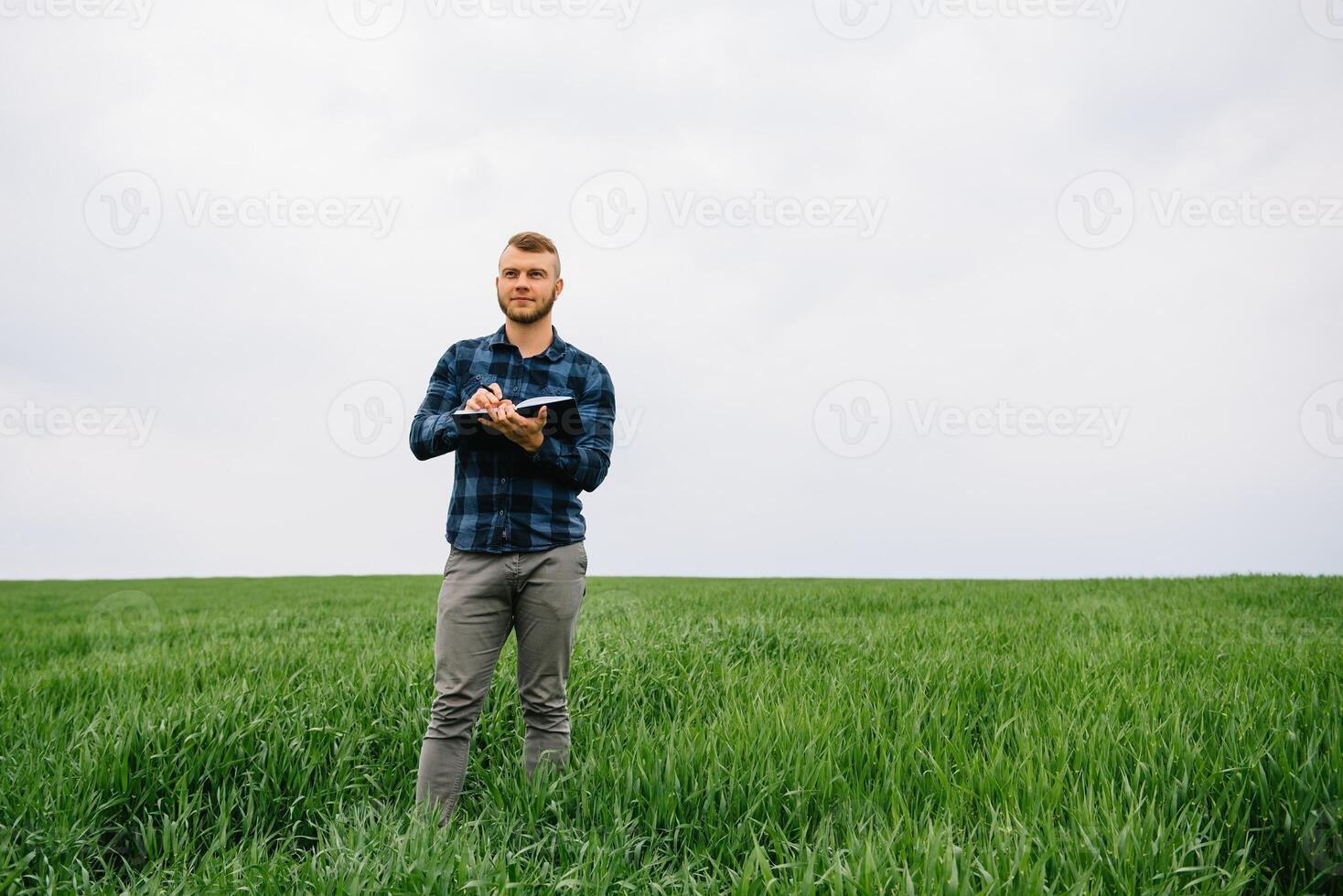 Young agronomist holds notebook in green wheat field. Agribusiness concept. agricultural engineer standing in a wheat field with a tablet in summer. photo