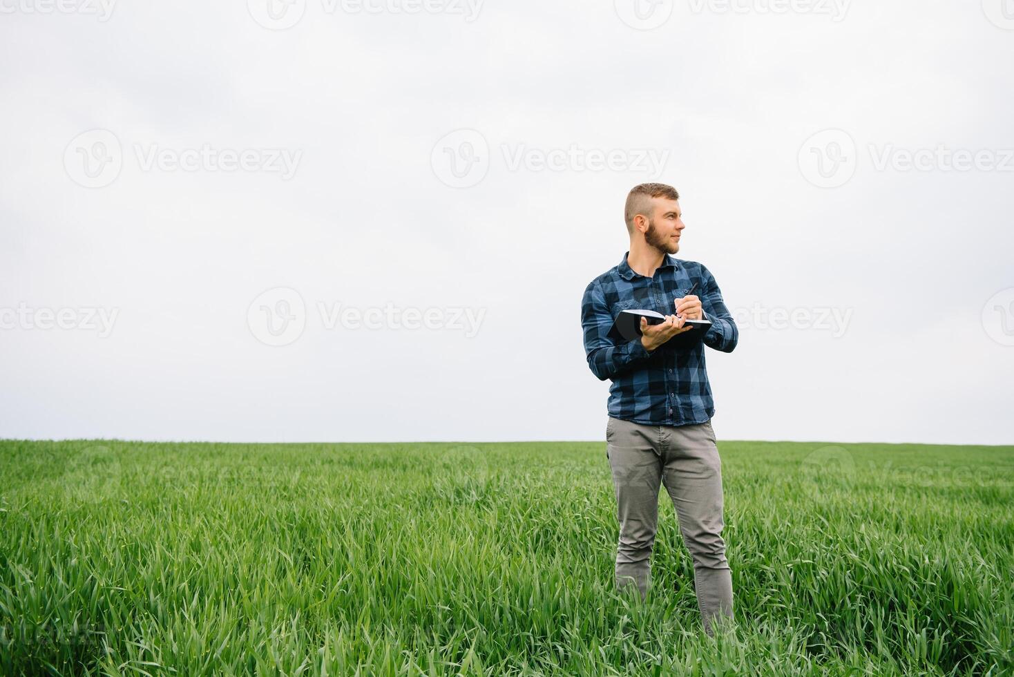 Young agronomist holds notebook in green wheat field. Agribusiness concept. agricultural engineer standing in a wheat field with a tablet in summer. photo