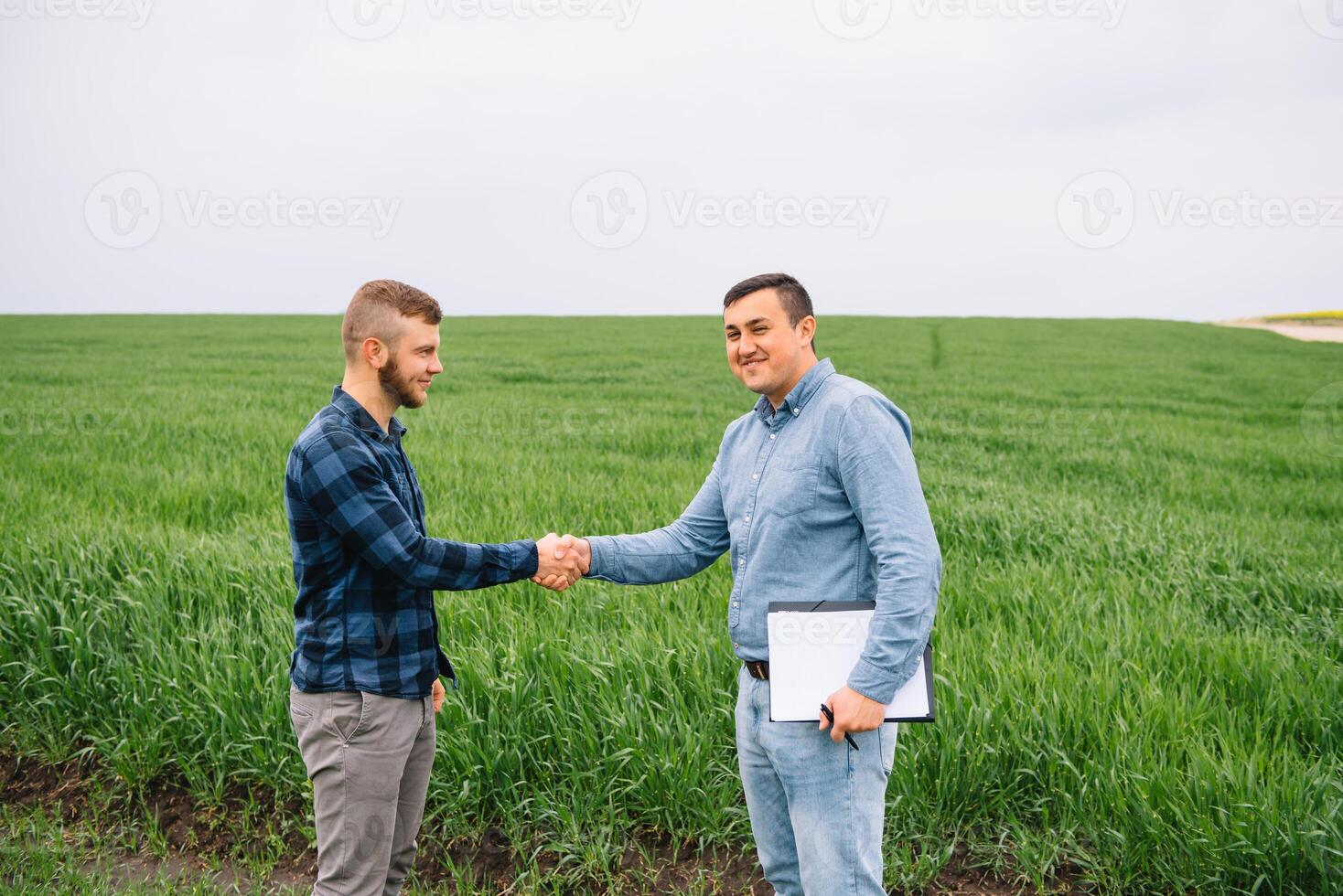 Two farmer standing in a green wheat field and shake hands. photo