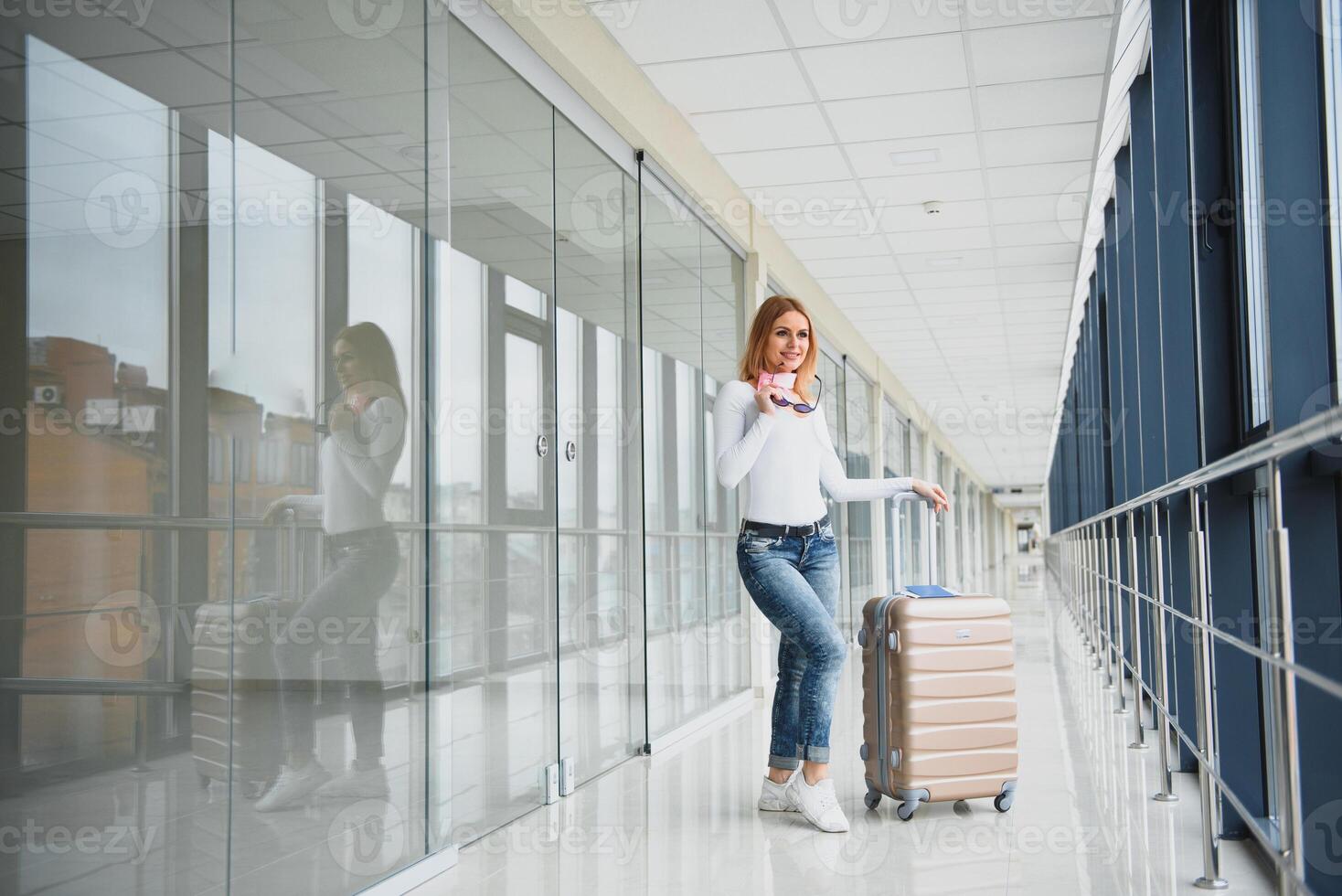 Casually dressed young stylish female traveller checking a departures board at the airport terminal hall in front of check in couters. Flight schedule display blured in the background. Focus on woman. photo
