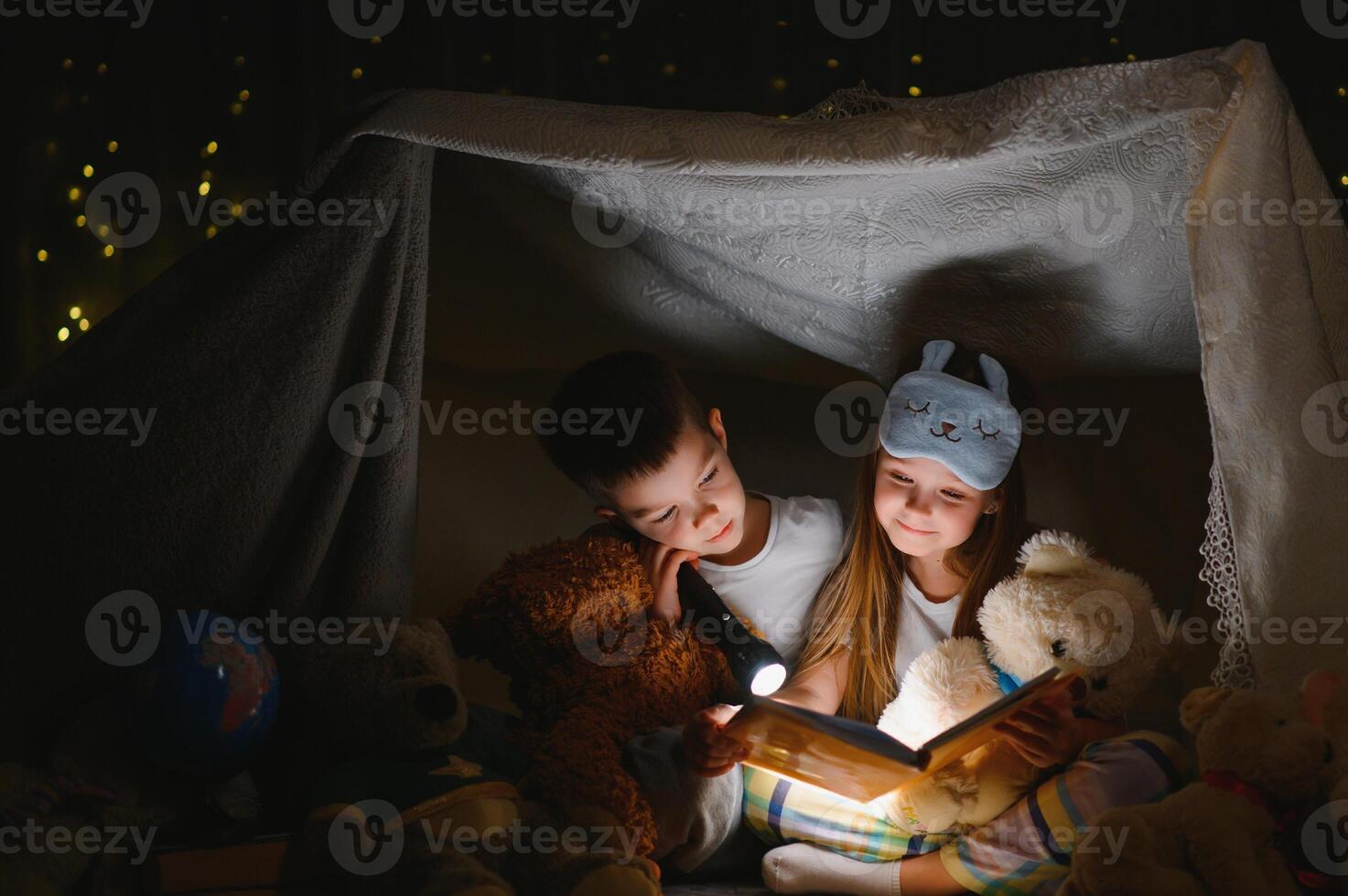 happy family children reading a book with a flashlight in a tent at home photo