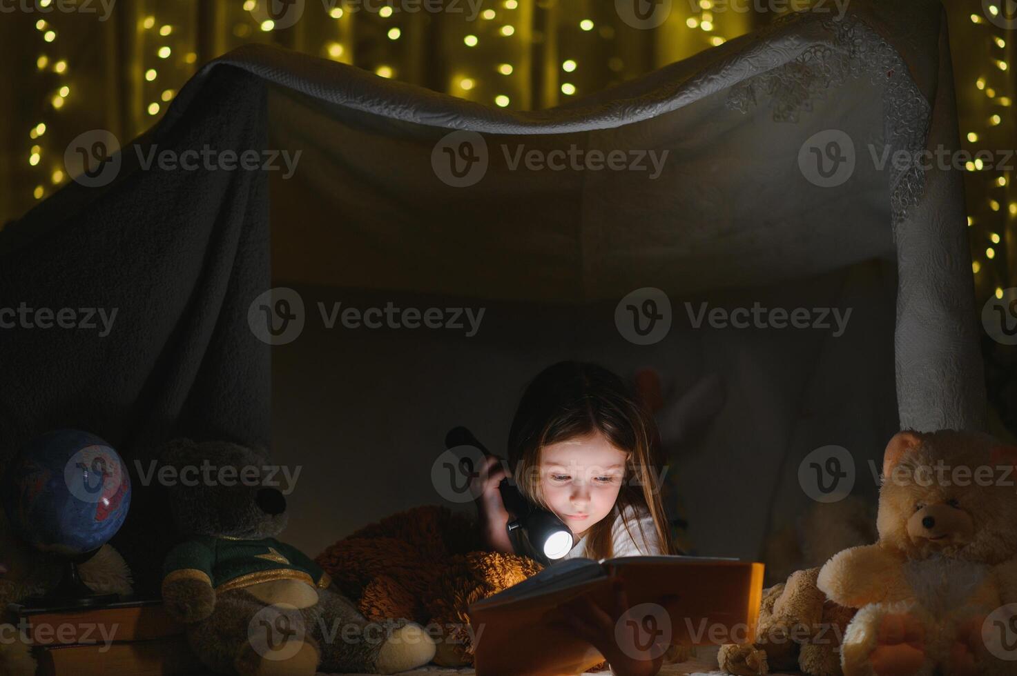 happy child girl laughing and reading book in dark in a tent at home photo