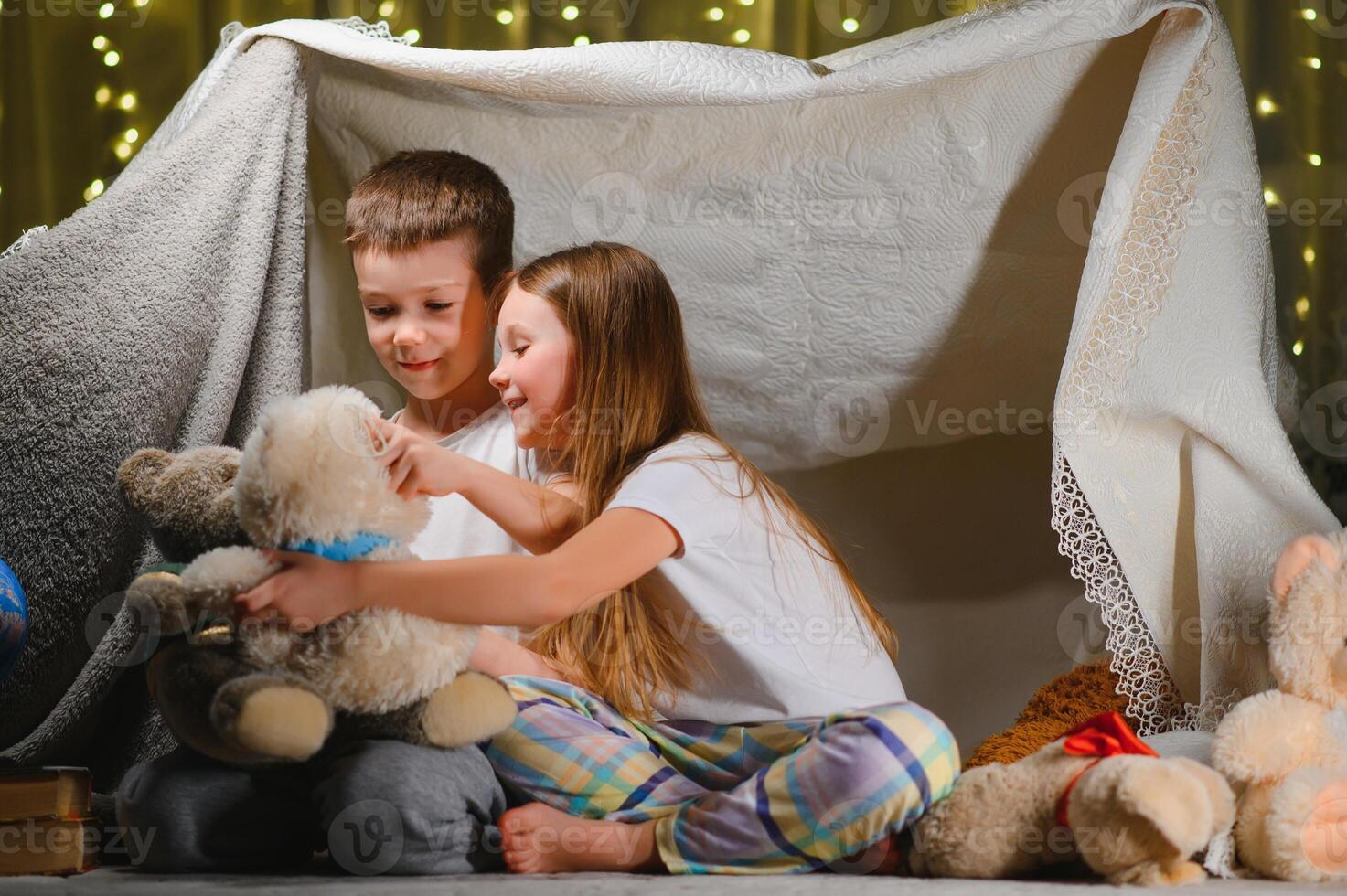 kids lying on floor in cozy nursery. Boy and girl holding flashlights in hands. Children play in a makeshift tent in the nursery. photo