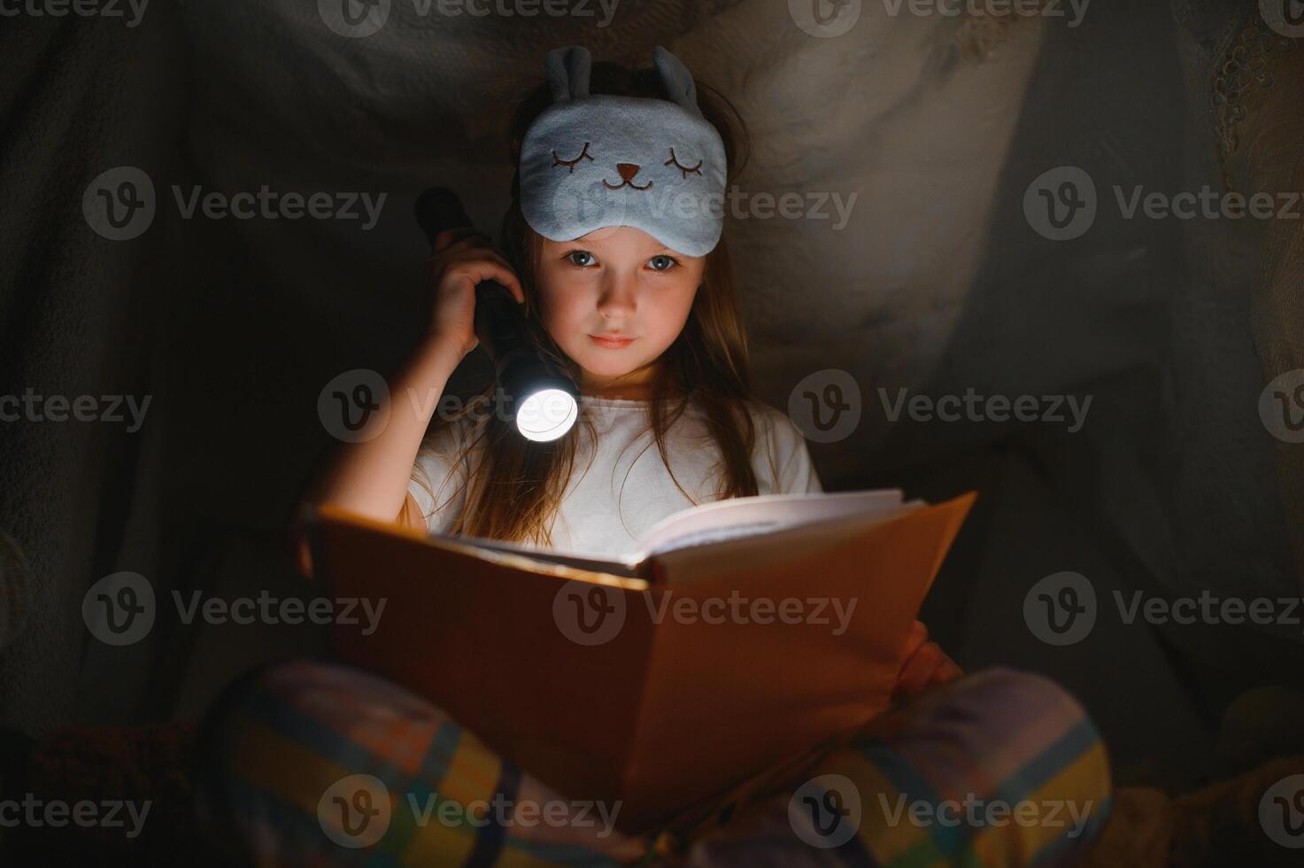happy child girl laughing and reading book in dark in a tent at home photo