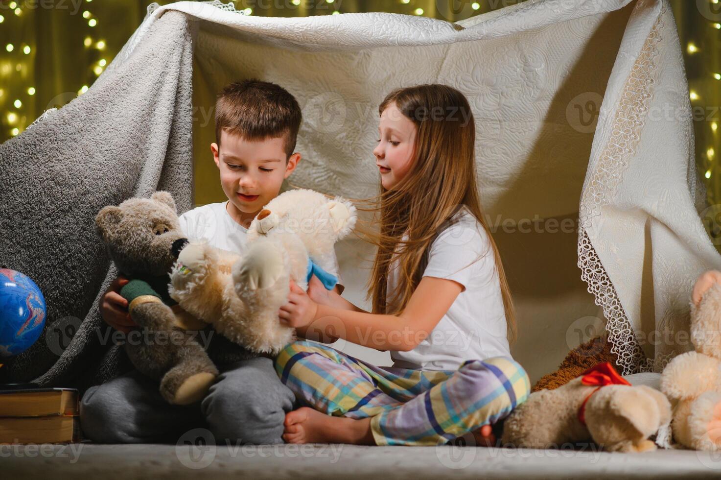 kids lying on floor in cozy nursery. Boy and girl holding flashlights in hands. Children play in a makeshift tent in the nursery. photo