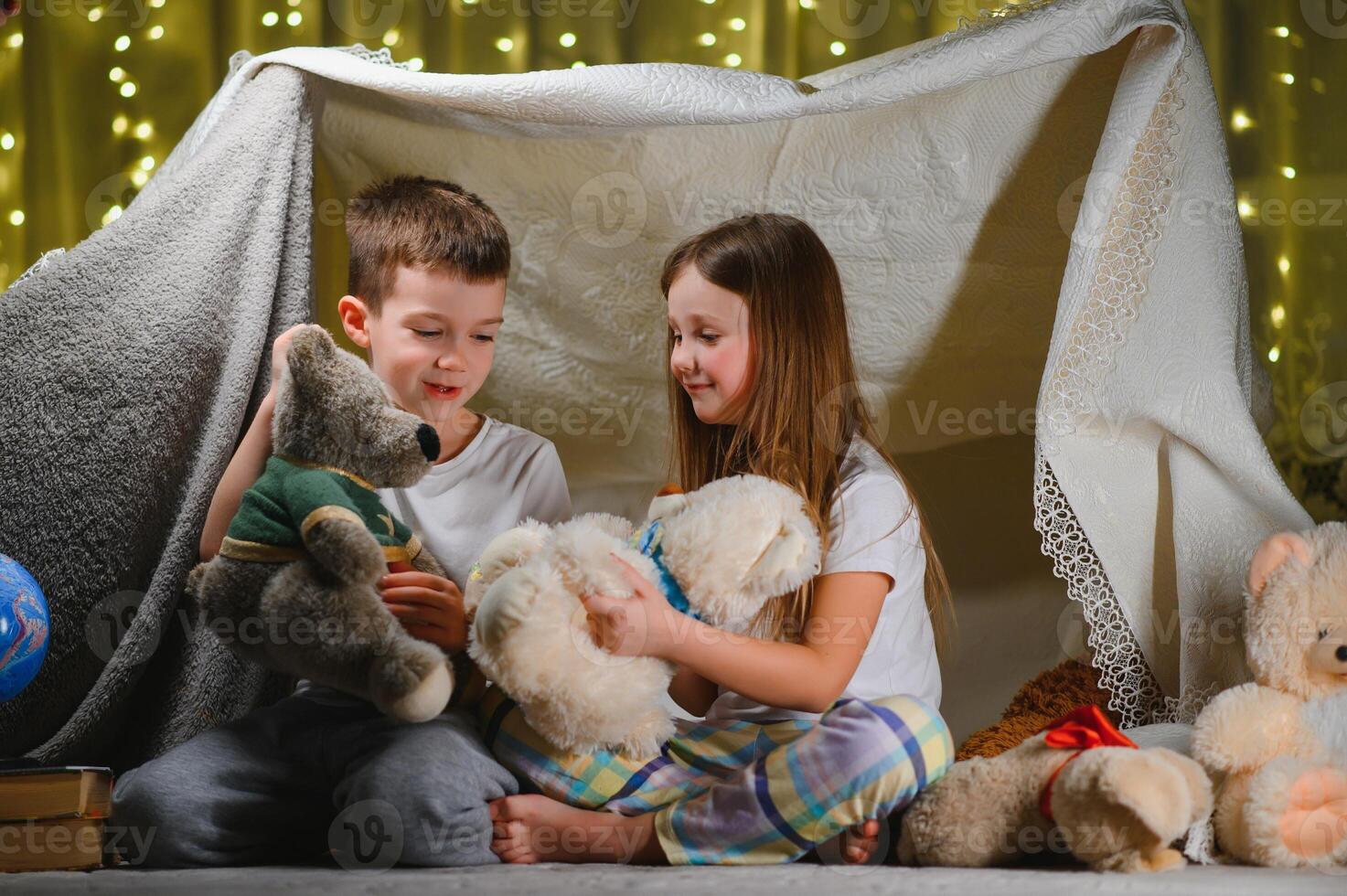 Two little child play at home in the evening to build a camping tent to read books with a flashlight and sleep inside. Concept of game, magic, creativity, alarm systems photo