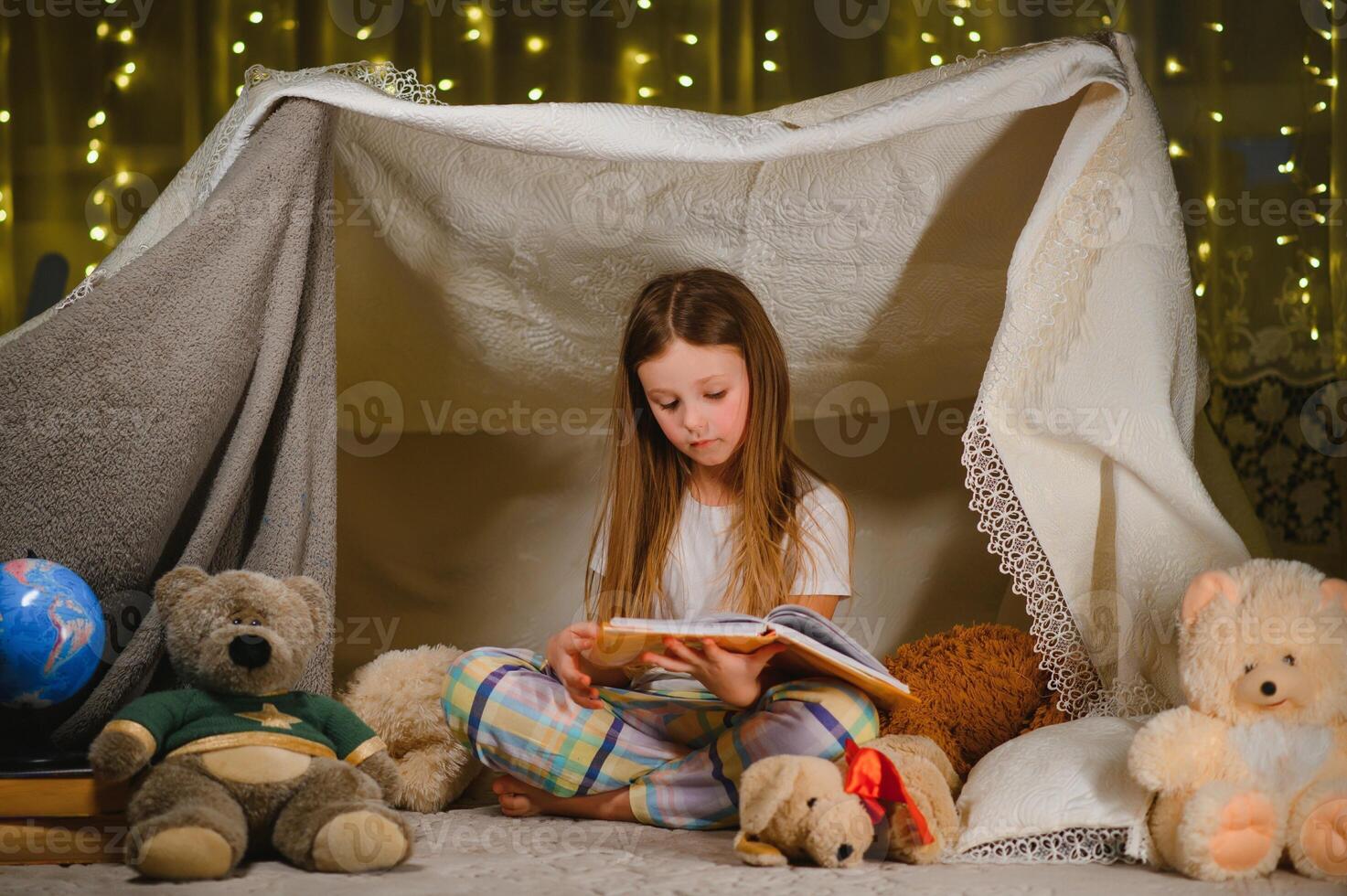 Reading and family games in children's tent. Little girl with books and flashlight before going to bed. photo