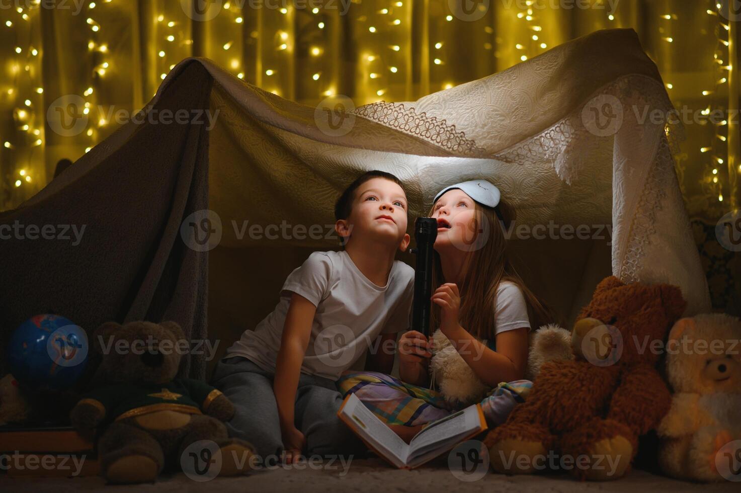 children boy and girl playing and frighten each other with flashlight in tent at night photo