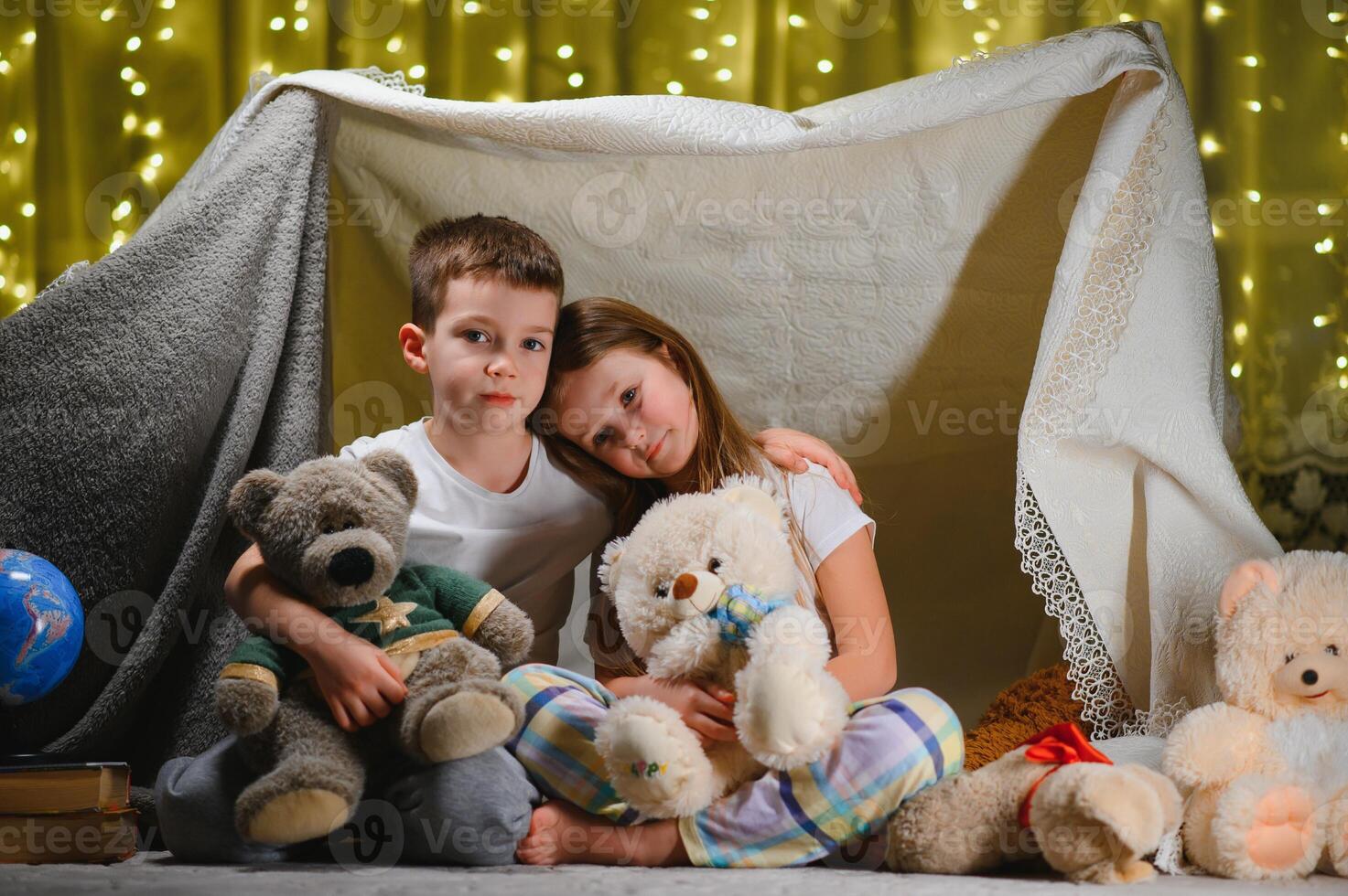 Two little children play at home in the evening to build a camping tent to read books with a flashlight and sleep inside. Concept of game, magic, creativity, alarm systems photo