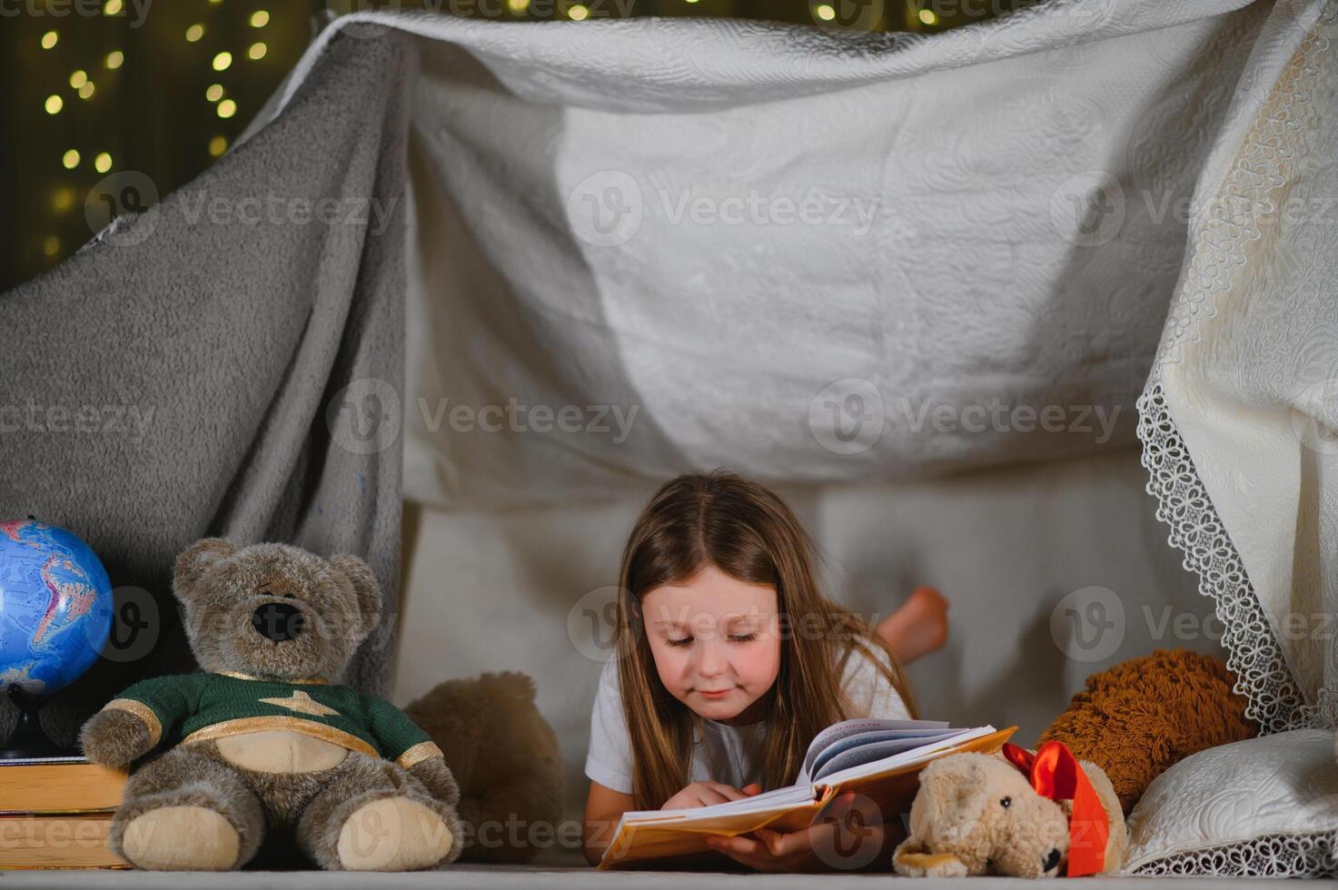 child girl reading with book and flashlight and teddy bear in tent. before going to bed photo
