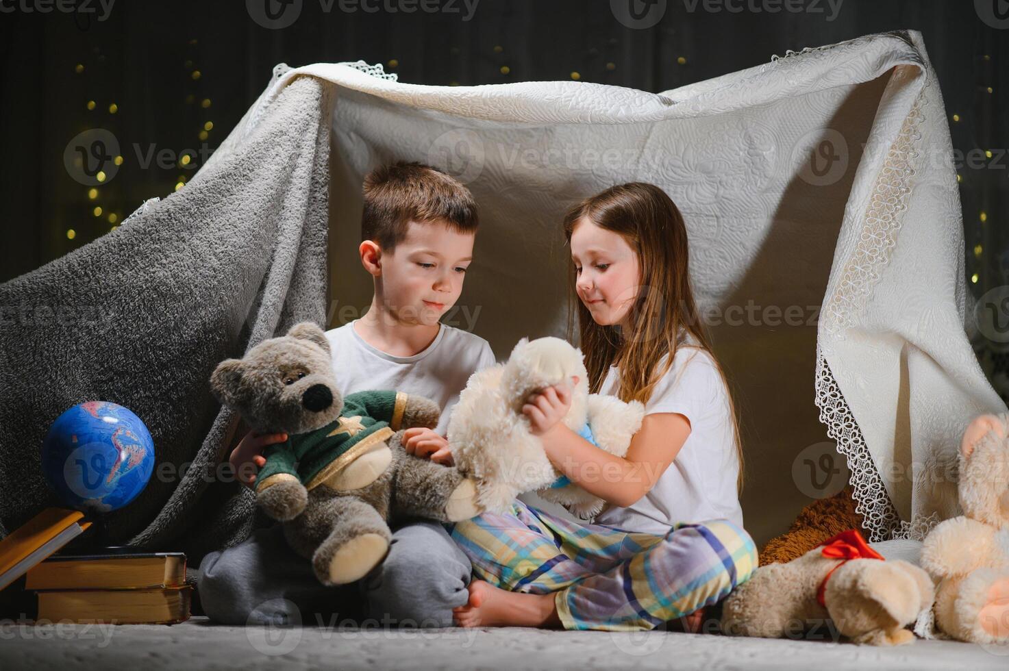 Two little child play at home in the evening to build a camping tent to read books with a flashlight and sleep inside. Concept of game, magic, creativity, alarm systems photo