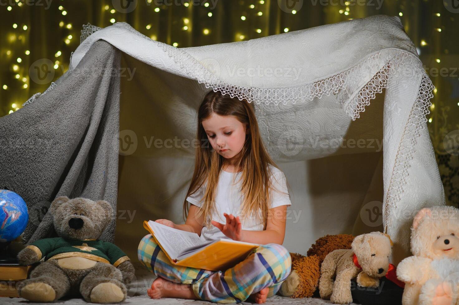 happy child girl laughing and reading book in dark in a tent at home photo