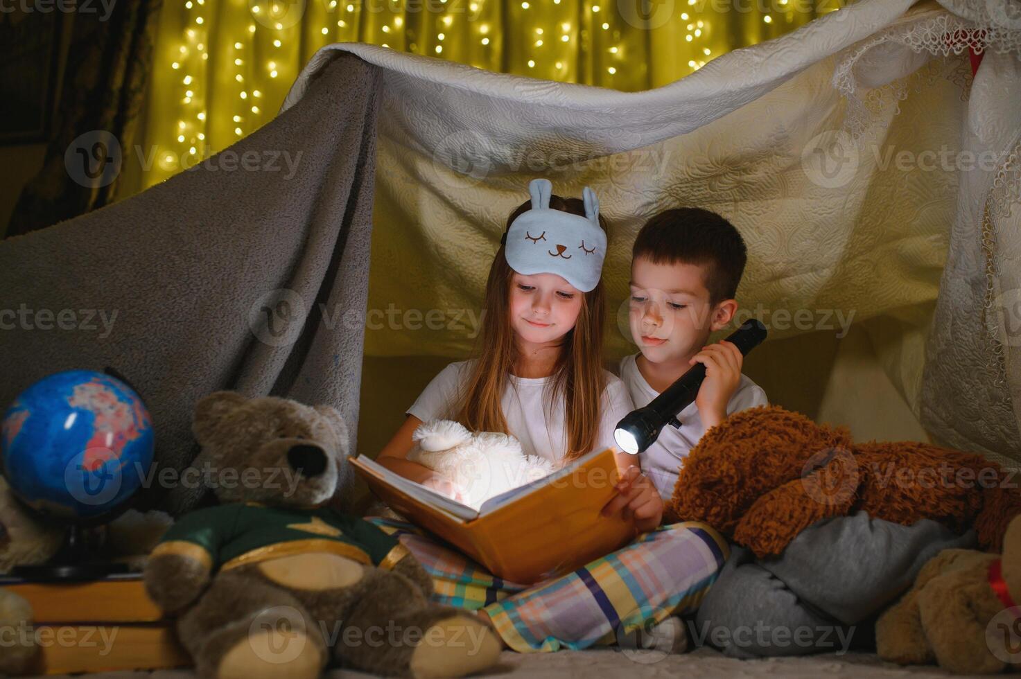 happy family children reading a book with a flashlight in a tent at home photo