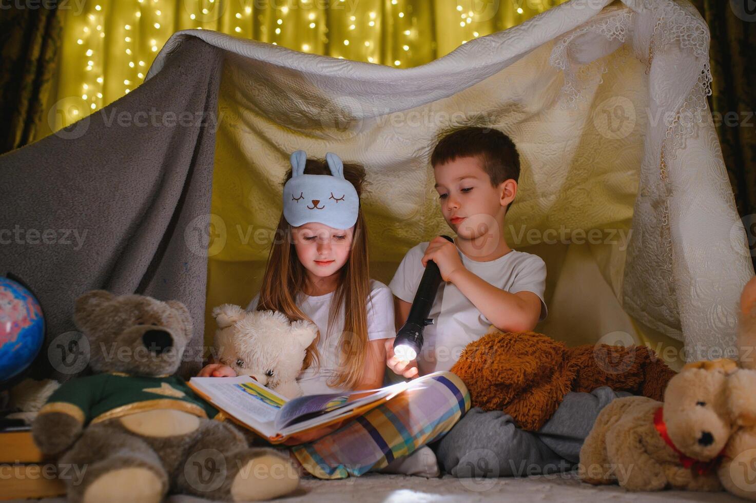reading and family games in children's tent. boy and girl with book and flashlight before going to bed photo