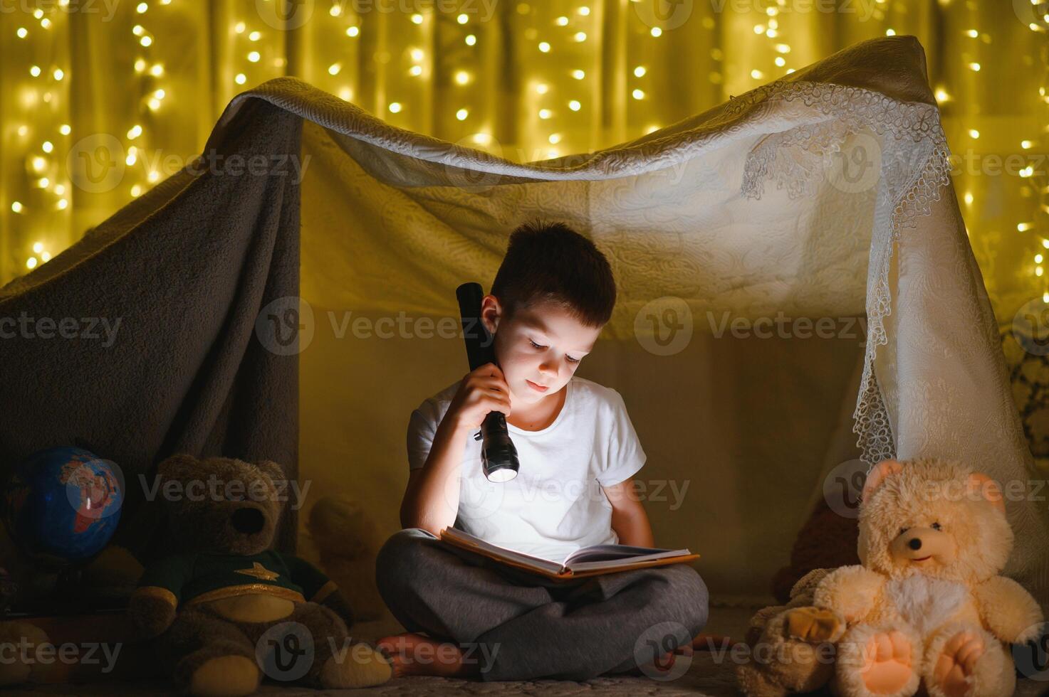 little boy reading book in play tent at night. photo