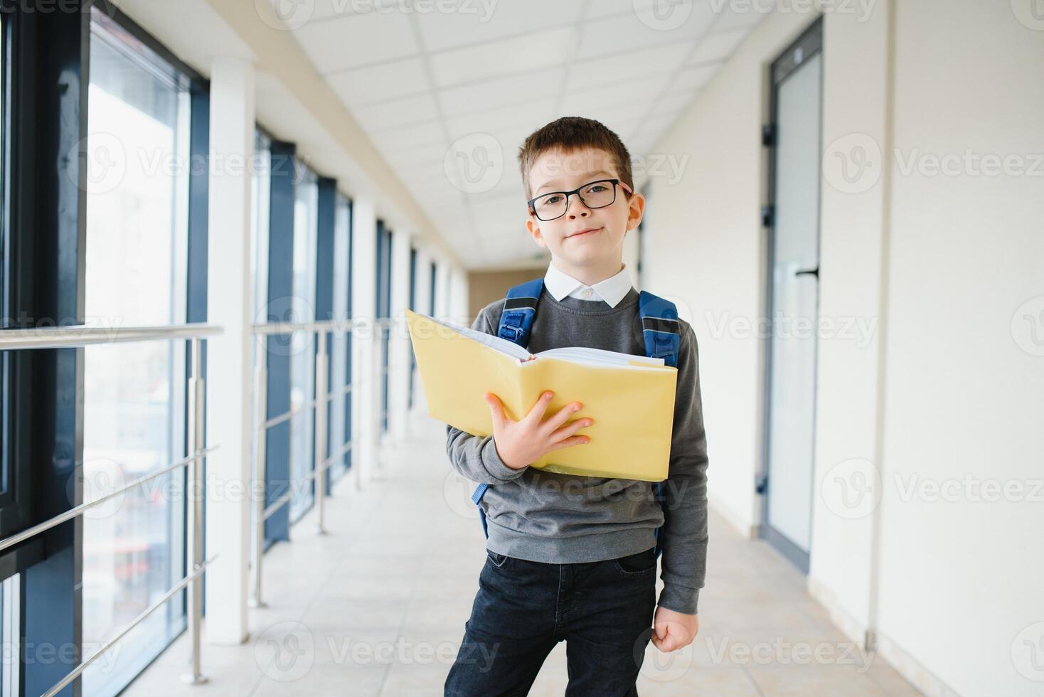 Portrait of happy school student. Smart elementary school kid glasses standing in school. Little child in holding a book photo