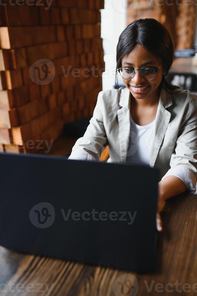 Happy african american woman worker using laptop work study at computer in loft office or cafe, smiling mixed race female student freelancer using pc app dating communicating online watching webinar photo