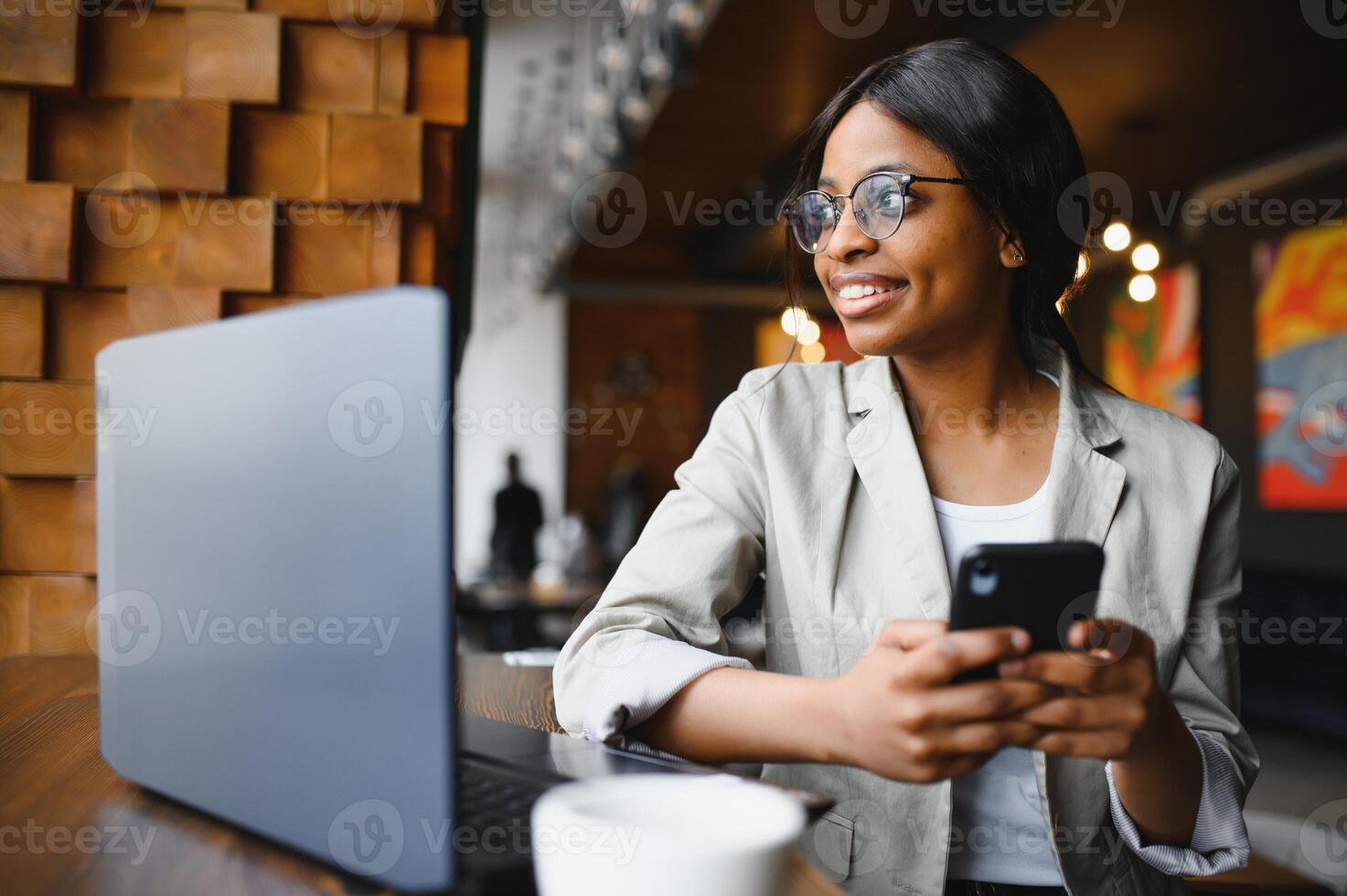 Beautiful african business woman waiting for the meeting in a co-working space and sitting with the portable computer. Hipster girl is surfing the web on a laptop during lunch. photo