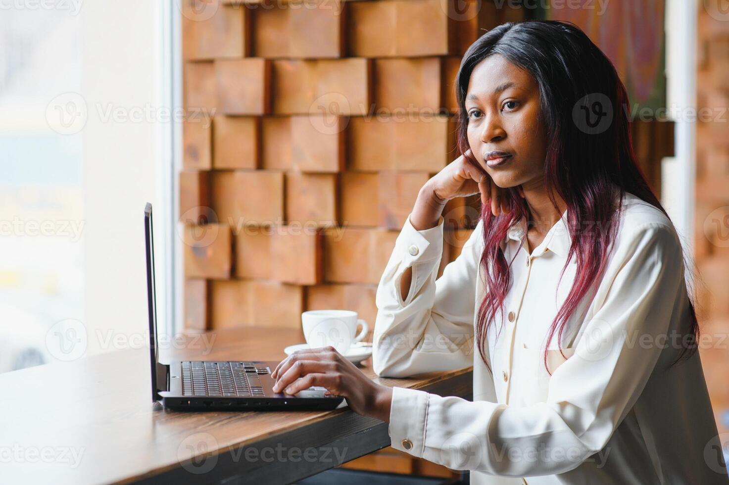 Beautiful african business woman waiting for the meeting in a co-working space and sitting with the portable computer. Hipster girl is surfing the web on a laptop during lunch. photo
