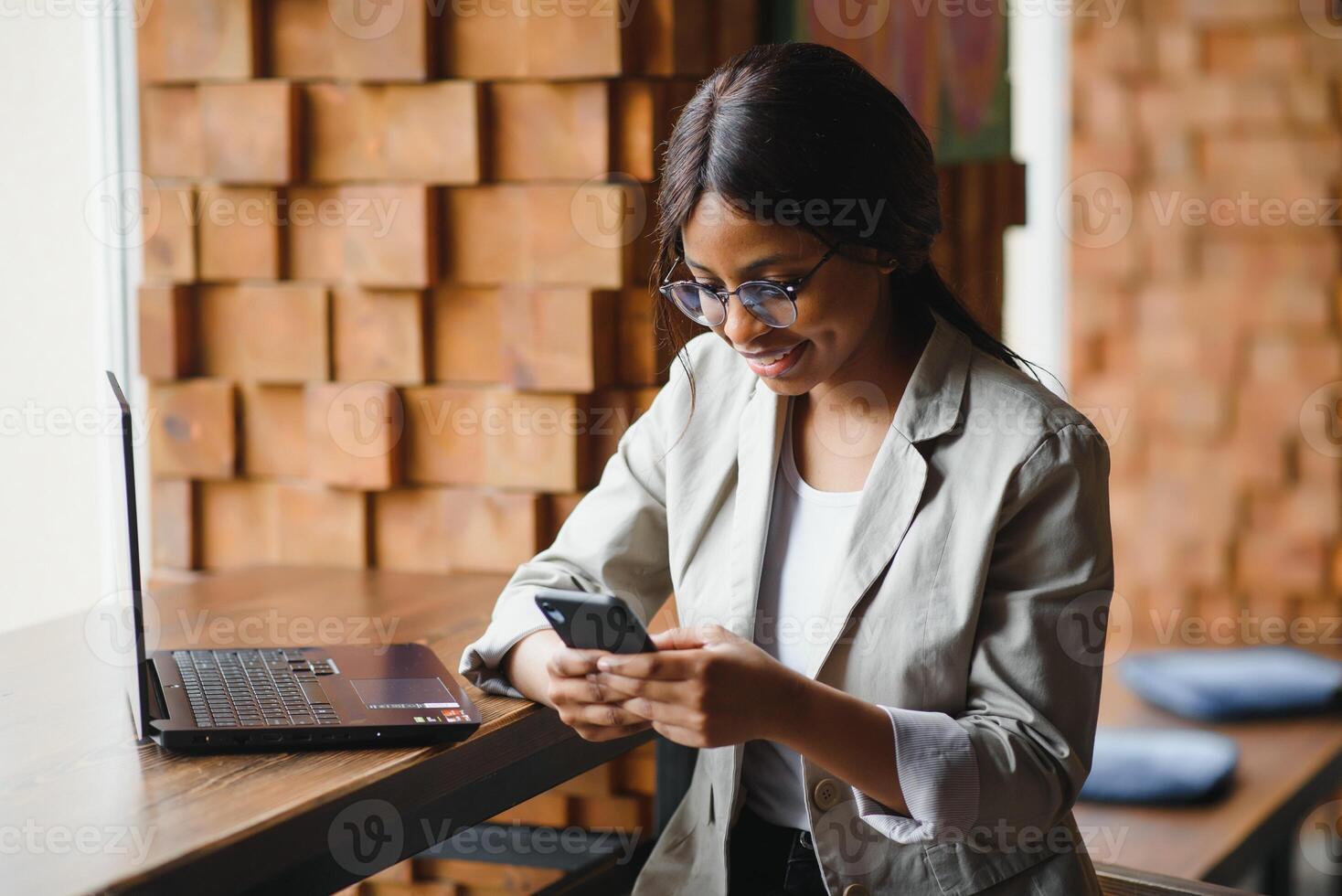 Young business woman is arranging the next business meeting in a modern coworking space by using a laptop. Young freelancer female is reading emails and other messages on a mobile phone. photo