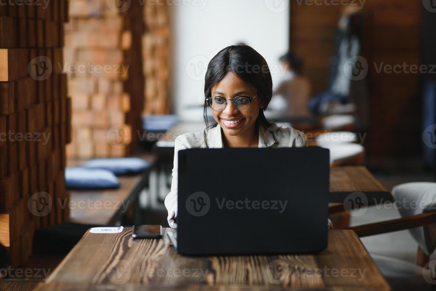 Beautiful african business woman waiting for the meeting in a co-working space and sitting with the portable computer. Hipster girl is surfing the web on a laptop during lunch. photo