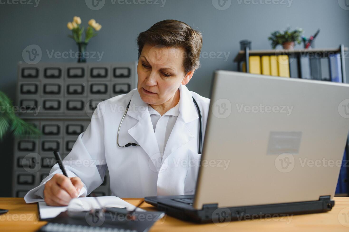 Portrait shot of middle aged female doctor sitting at desk and working in office. photo