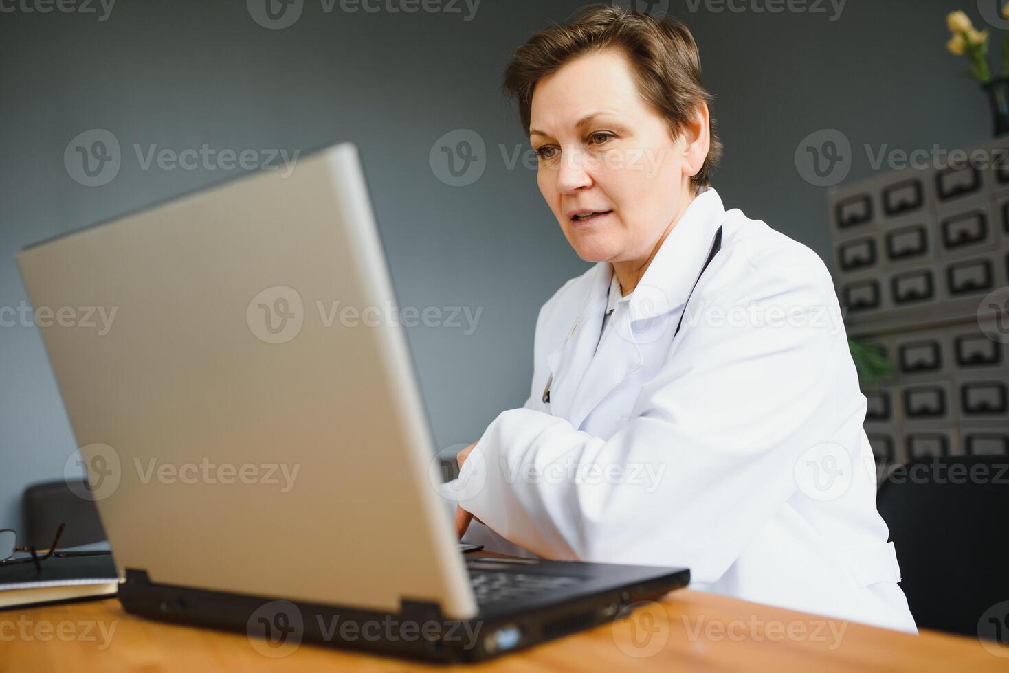 Portrait of female doctor counseling patient via call. Professional physician in white lab coat gesturing and explaining course of treatment sitting at office desk during online consultation. photo