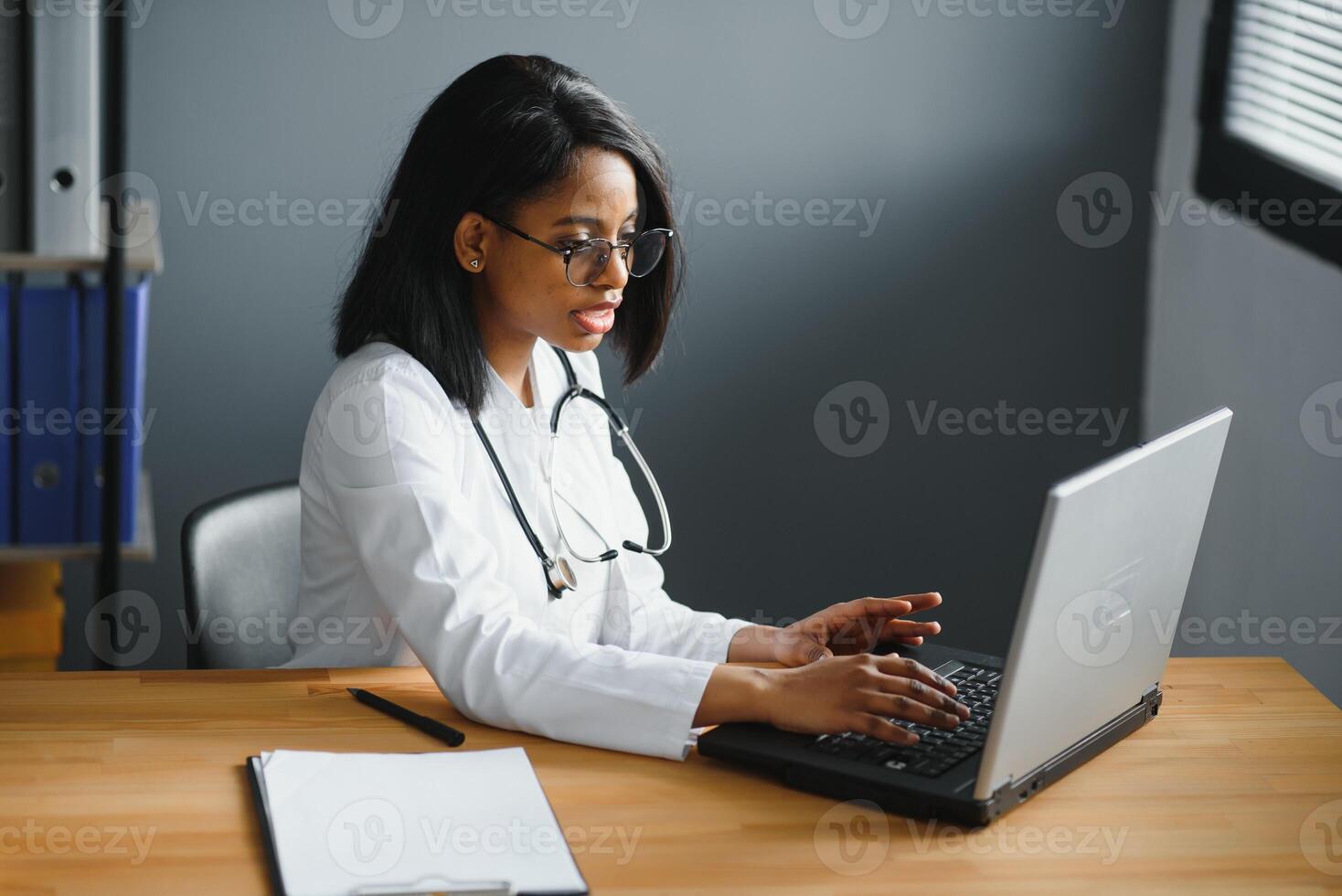 Portrait of young indian doctor working in the hospital while looking at laptop and write on clipboard. photo