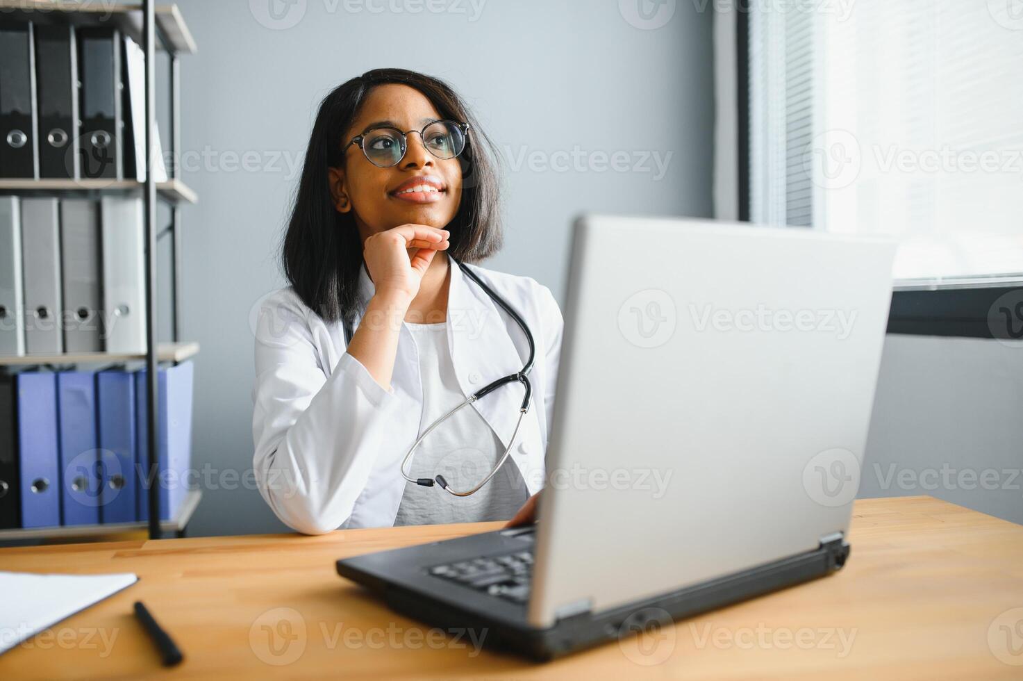 Portrait of young indian doctor working in the hospital while looking at laptop and write on clipboard. photo
