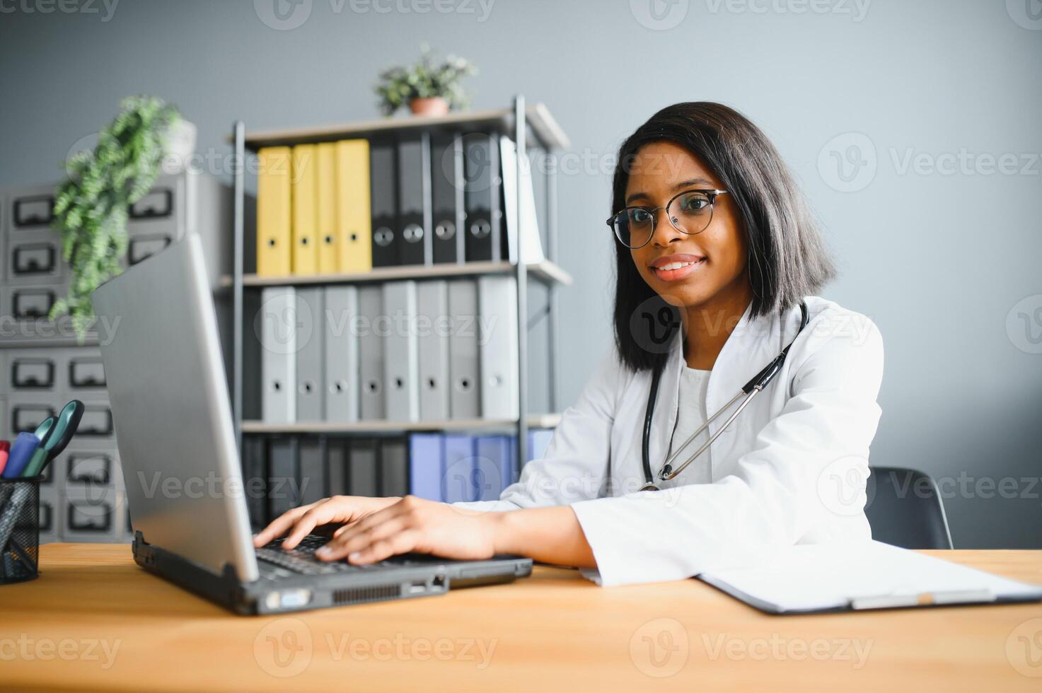Portrait of young indian doctor working in the hospital while looking at laptop and write on clipboard. photo