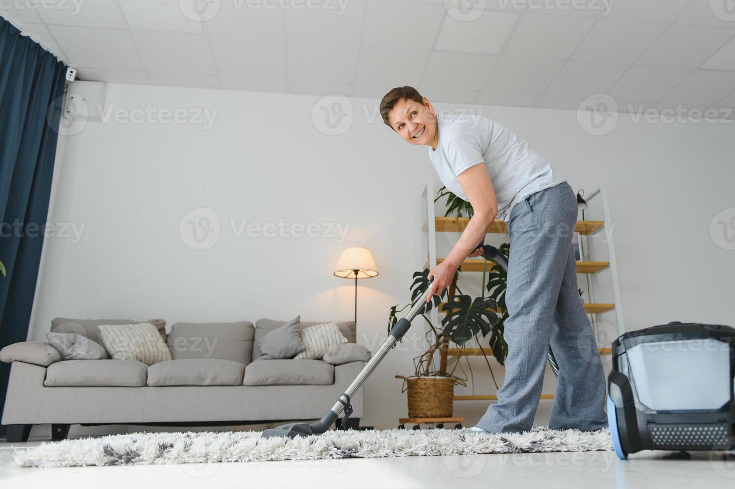 Portrait of senior woman with vacuum cleaner indoors at home, hoovering photo